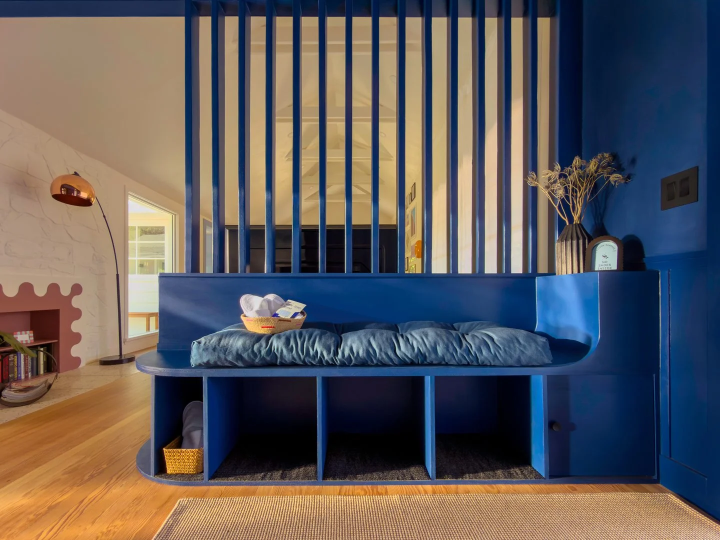 View of a blue partition with open shelving underneath in a living room, with a couch, a basket with clothes, and a lamp in the background.