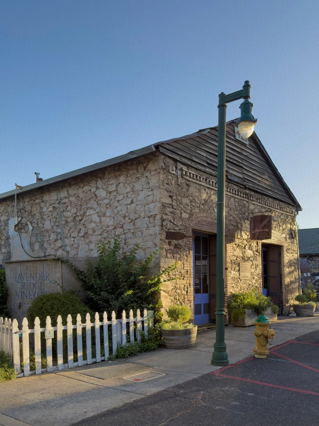 Stone building with a wooden roof, street lamp, and potted plants outside.