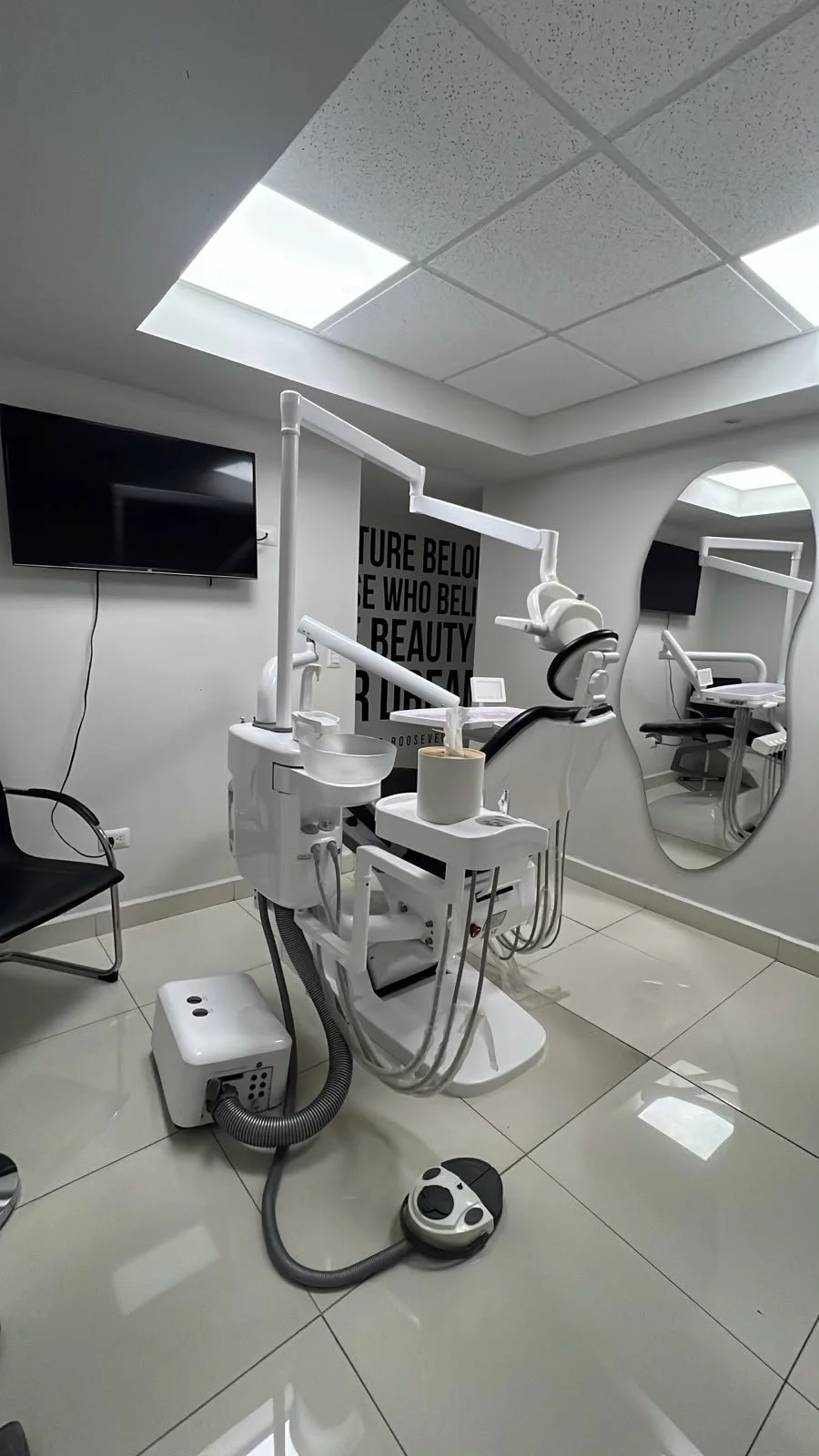 Dental treatment room featuring a dental chair, mirror, and wall-mounted TV.
