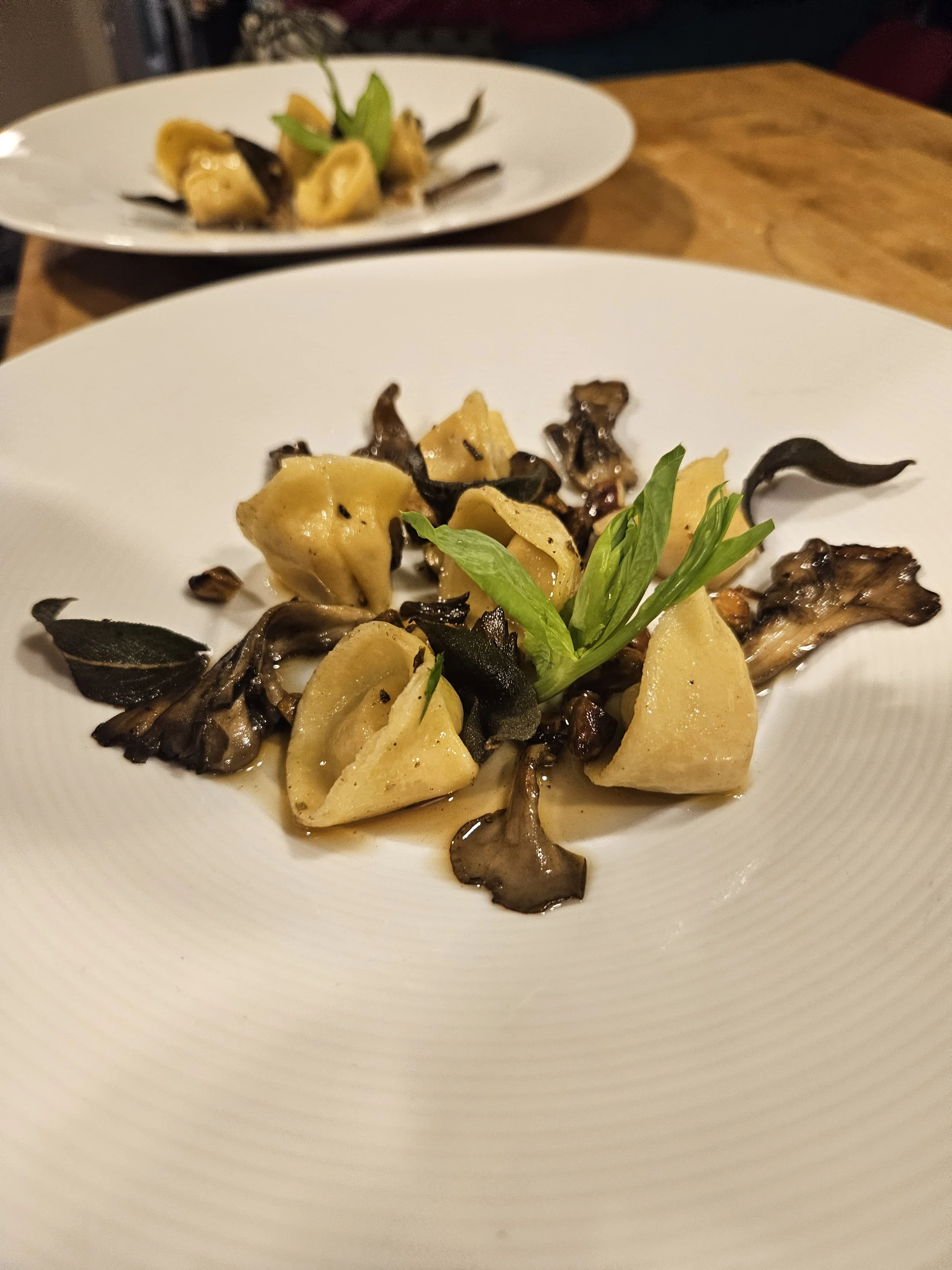 A white plate with pasta and black truffle slices, garnished with fresh herbs, placed on a wooden table.