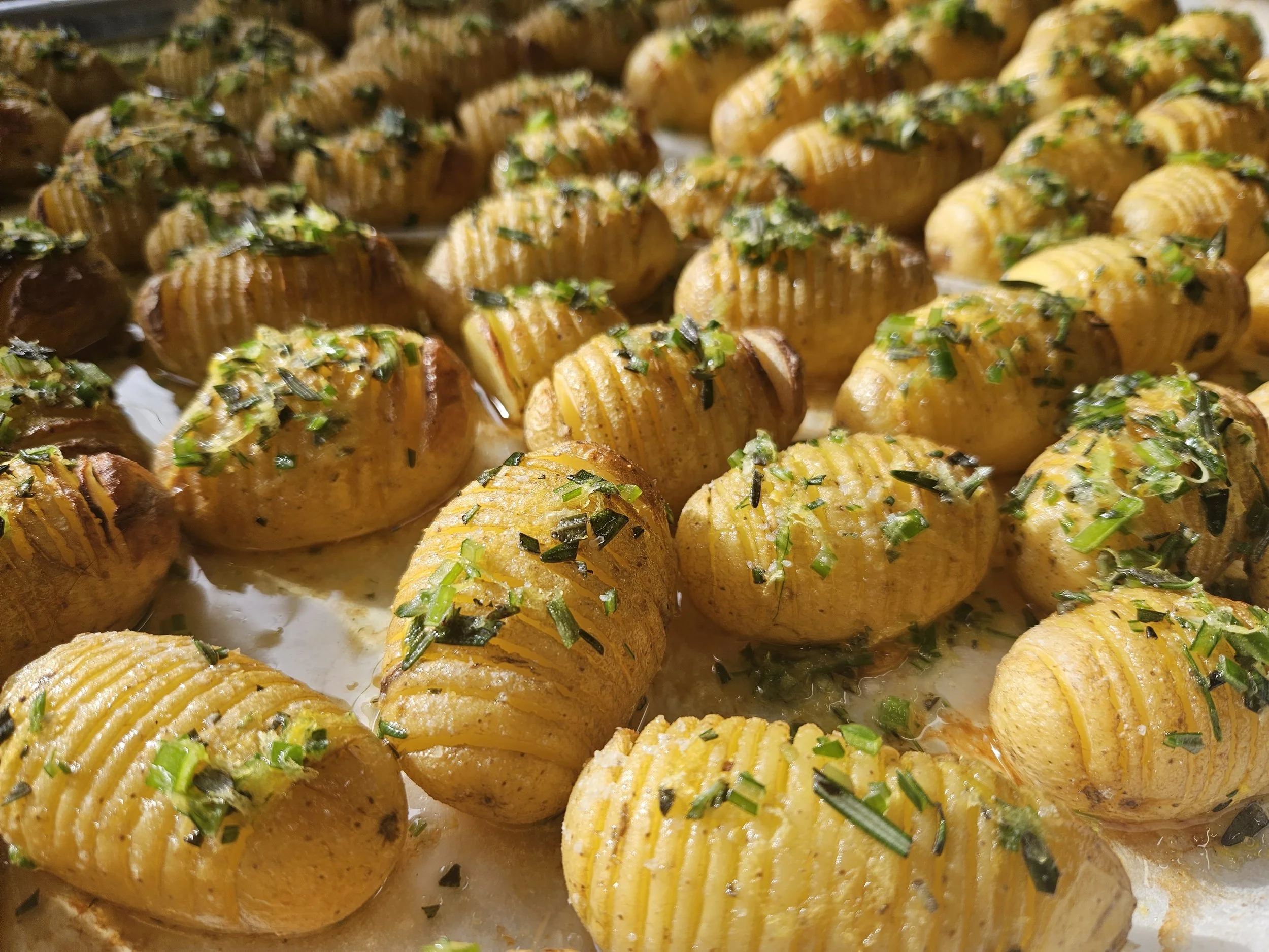 Close-up of roasted potatoes topped with chopped green herbs, possibly chives, on a tray.