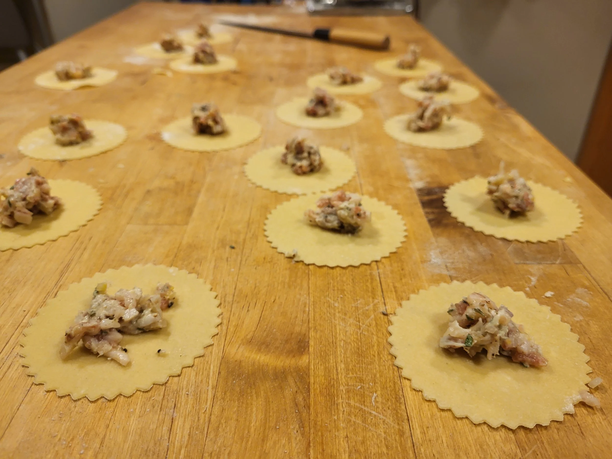 Uncut pasta with filling, arranged on a wooden surface, with a rolling pin nearby, preparing for ravioli.