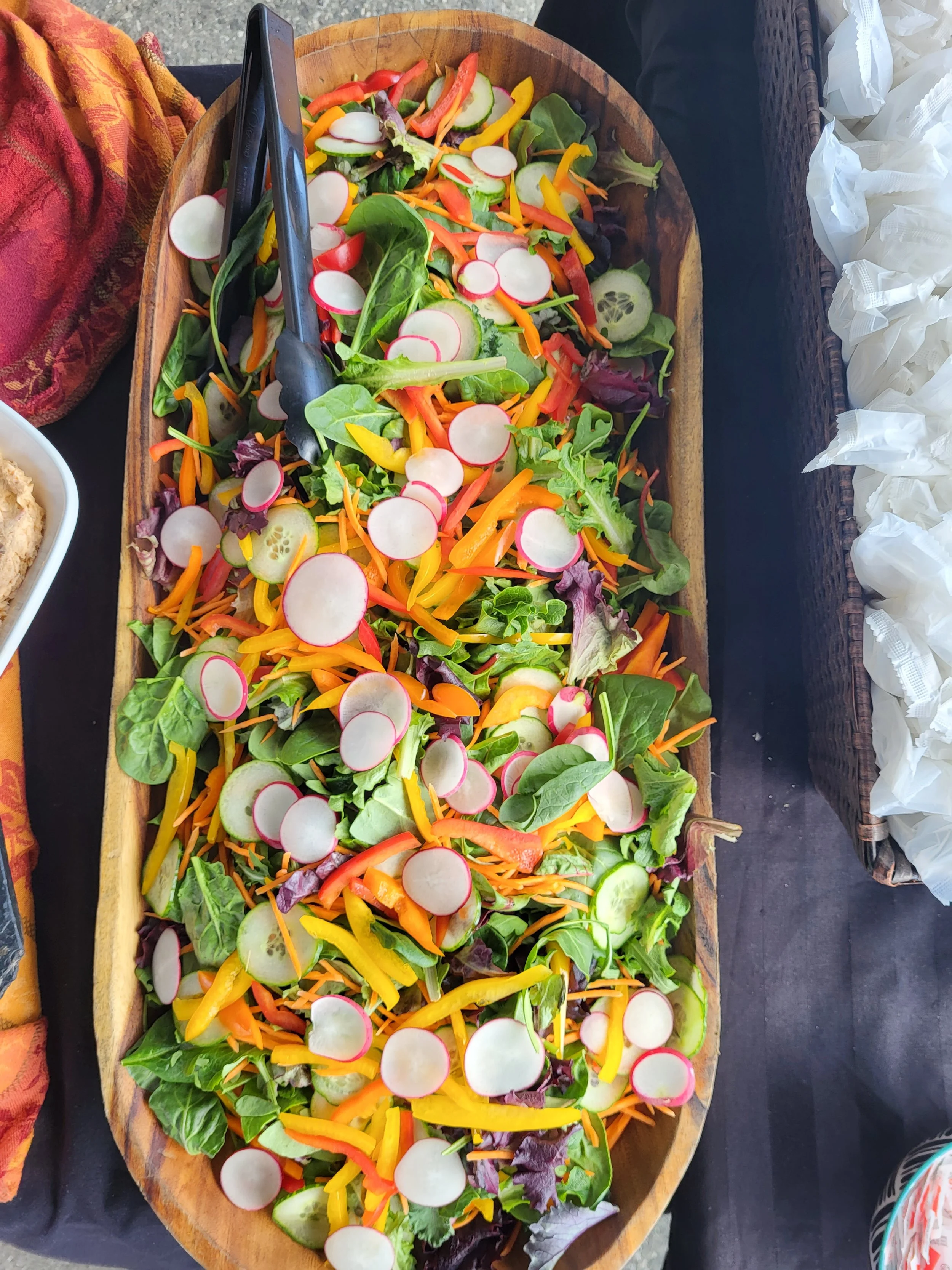Colorful mixed salad with sliced radishes, cucumbers, shredded carrots, bell peppers, and leafy greens in a wooden serving dish.