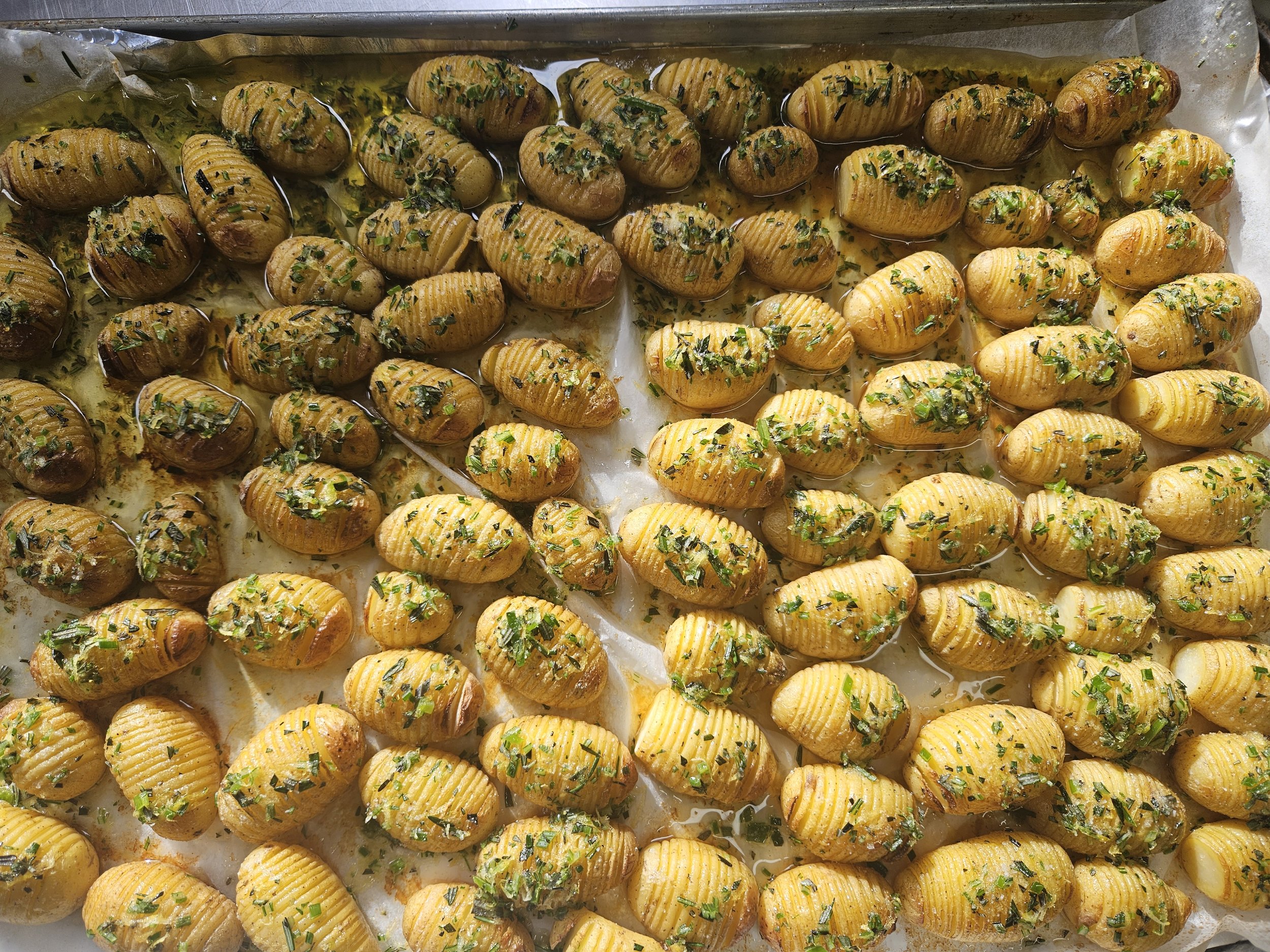 Baked potatoes topped with chopped herbs served on a tray.