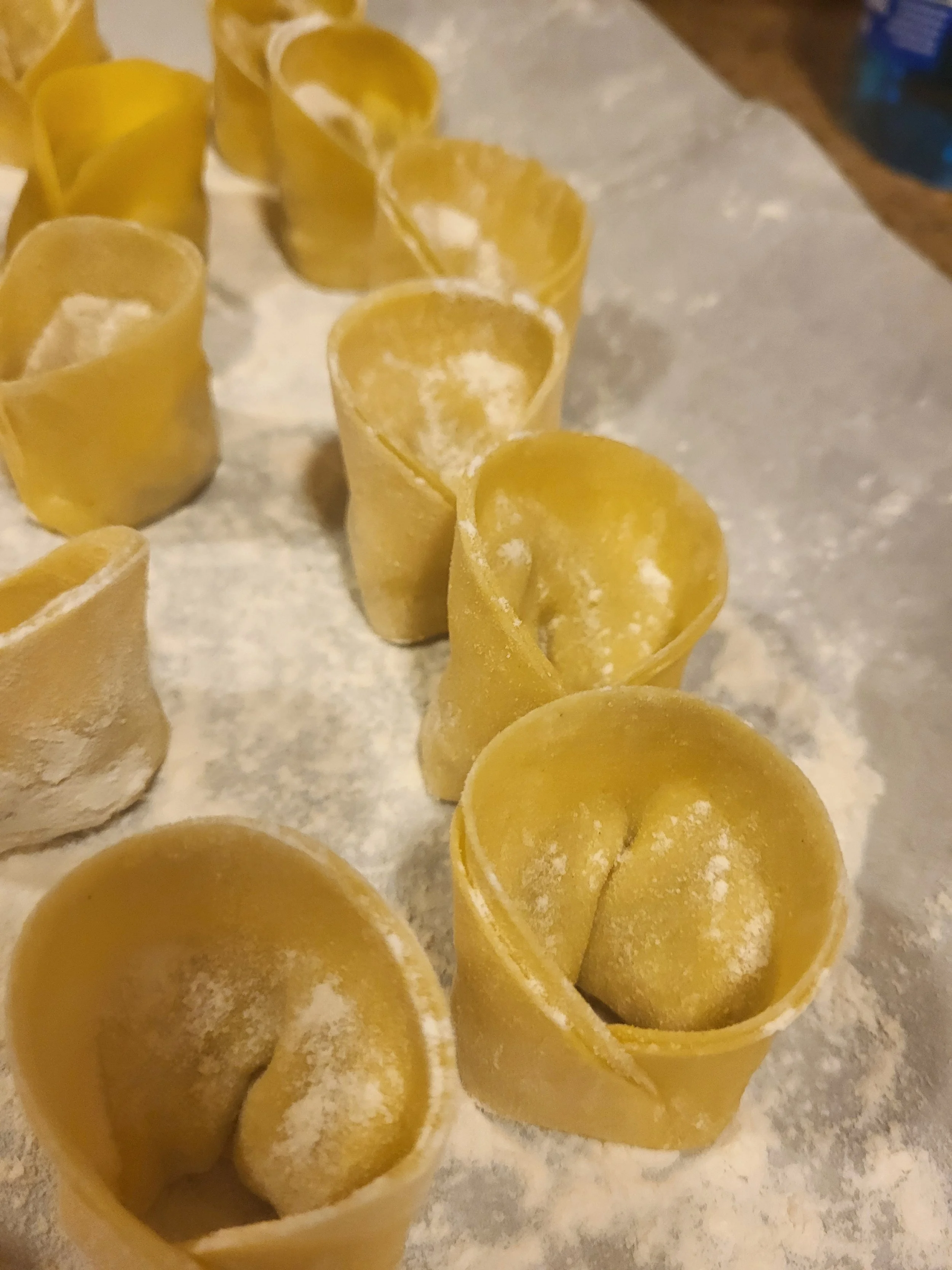 Fresh homemade pasta dough shaped into small pasta pieces, dusted with flour, on a floured surface.