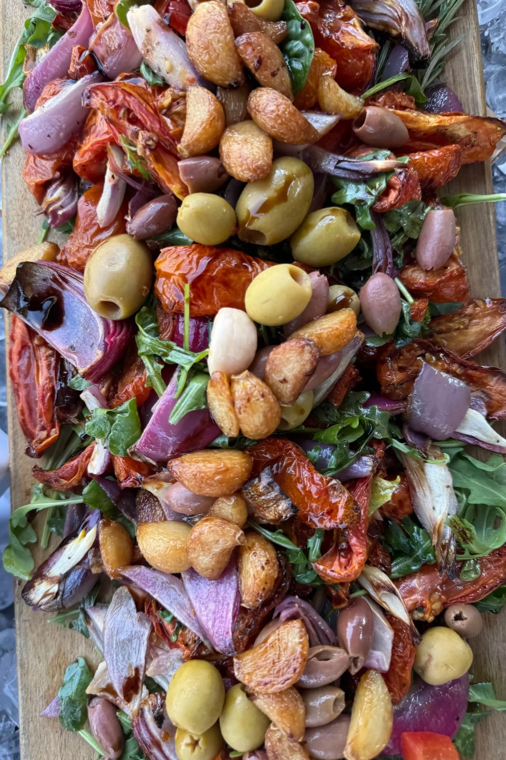 A platter of assorted roasted vegetables, including cherry tomatoes, potatoes, olives, onions, and leafy greens.