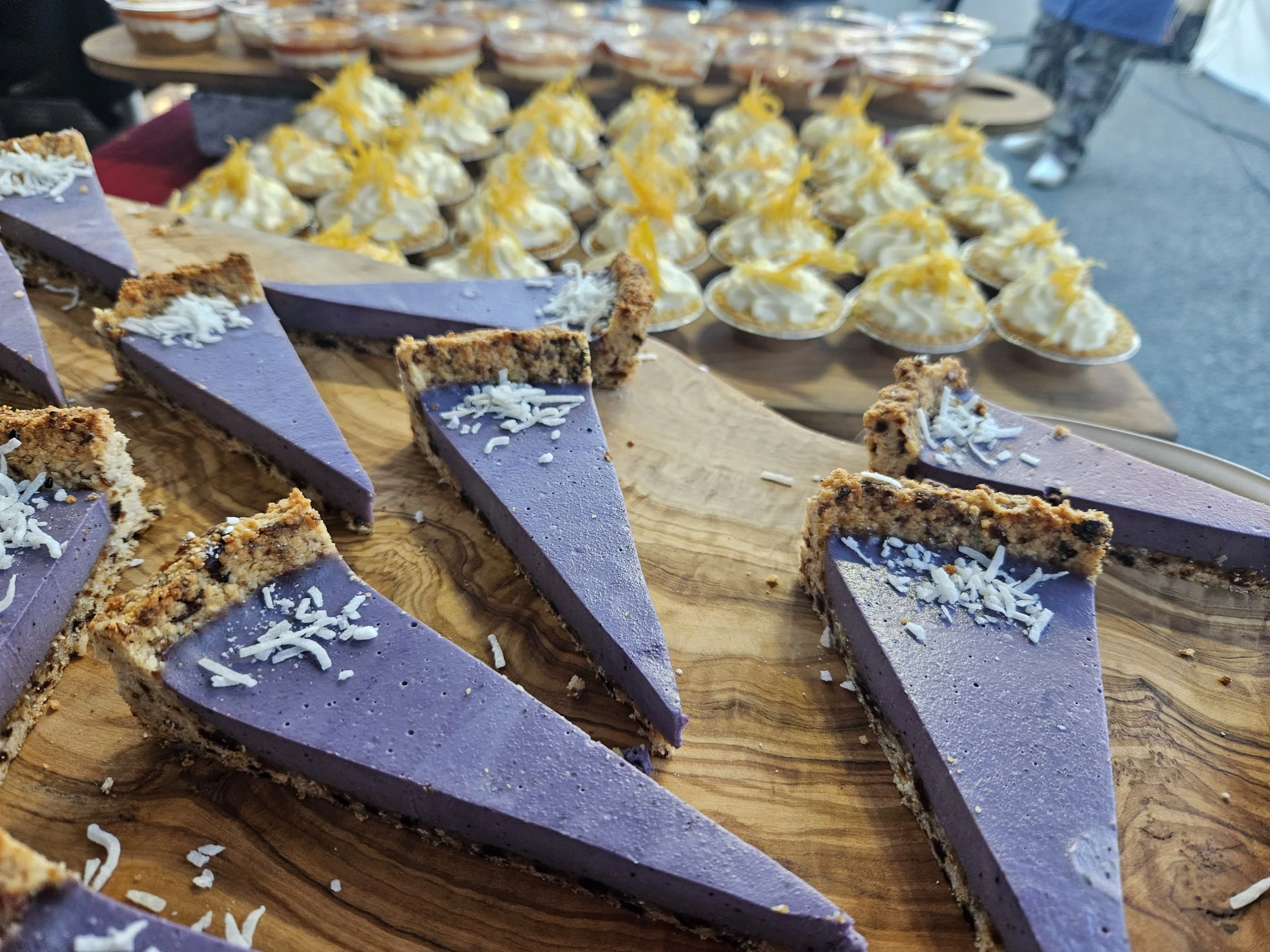 Close-up of sliced purple cheesecake with white shredded topping on a wooden platter.