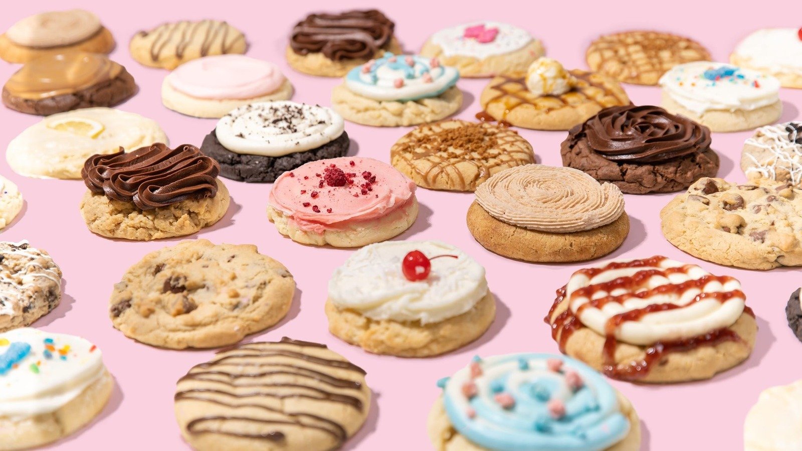 An assortment of decorated cookies with various frosting and toppings on a pink background.