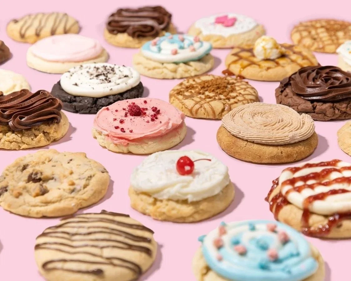 Assorted decorated cookies with various frosting, sprinkles, and toppings on a pink background.