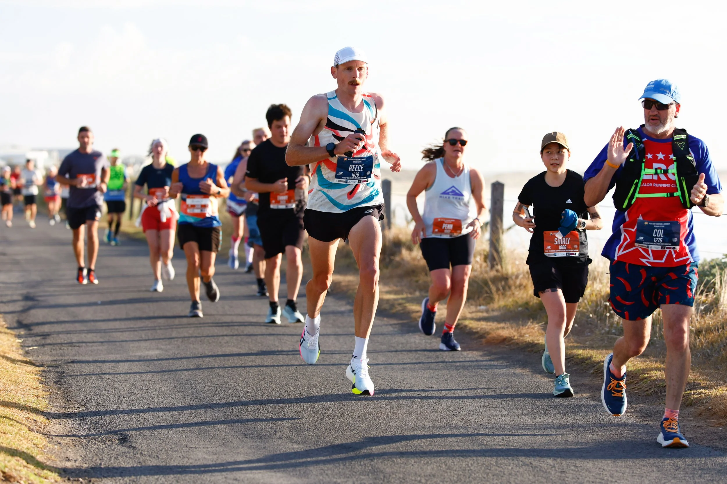 Group of runners participating in the Port Fairy Marathon on an outdoor path with a clear sky.