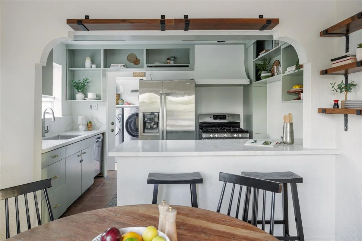Modern kitchen with open shelves, stainless steel appliances, a white marble countertop, and a wooden dining table with black chairs.