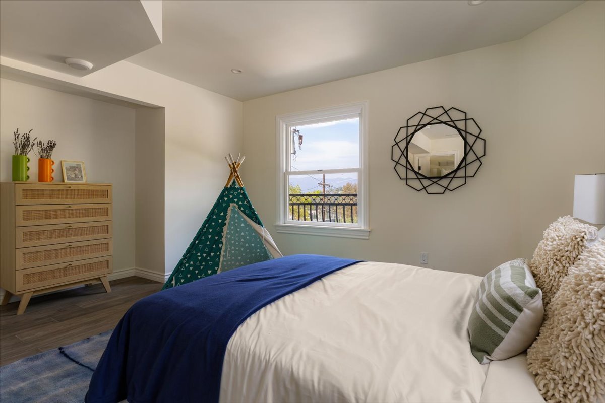 A bedroom with a bed covered in white and blue bedding, pillows, a decorative mirror on the wall, a small tent in the corner, and a dresser with vases and a picture frame.