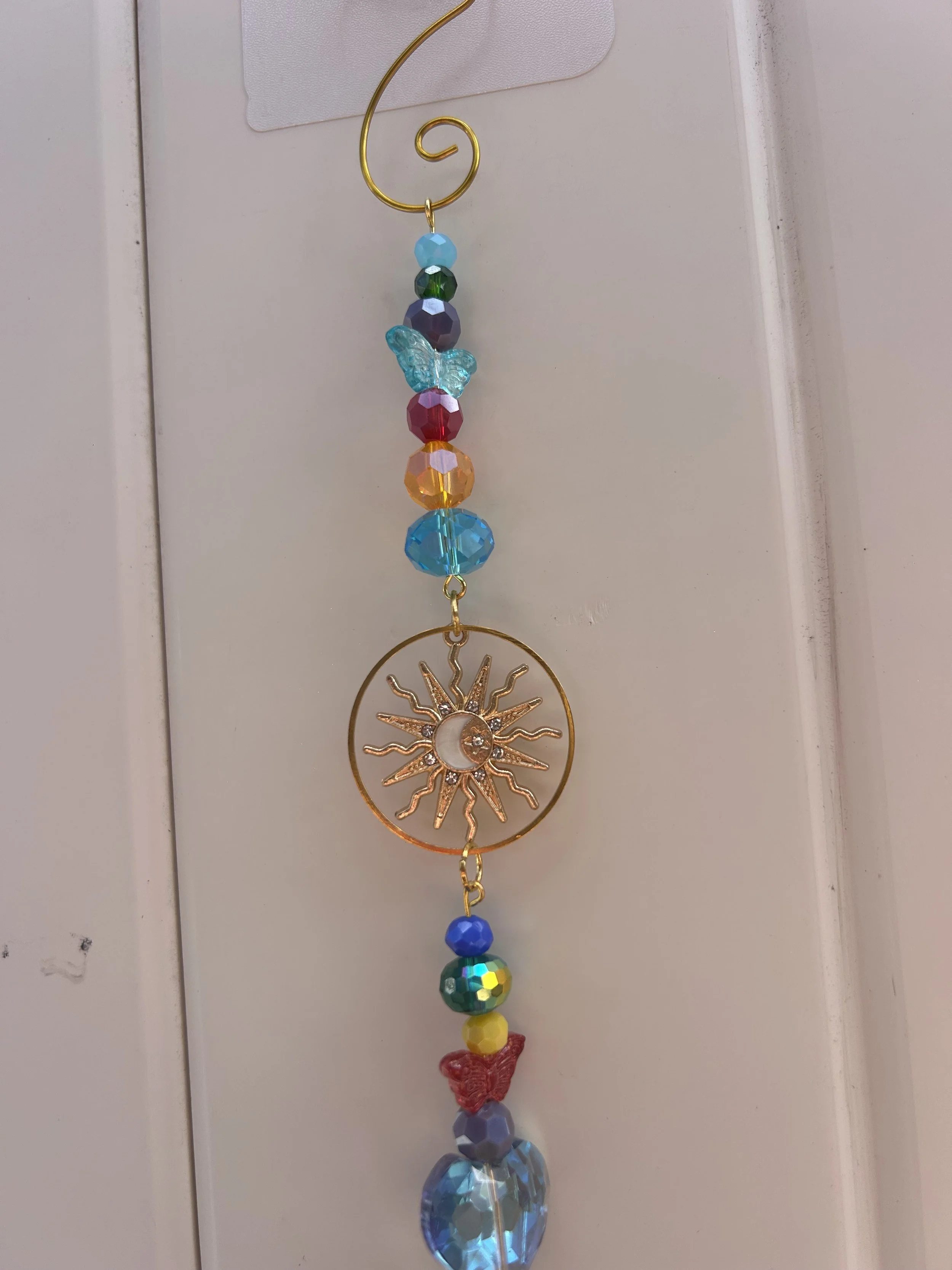 A colorful dangling decoration with beads, a butterfly, and a sun-shaped metal ornament, hanging vertically against a white background.
