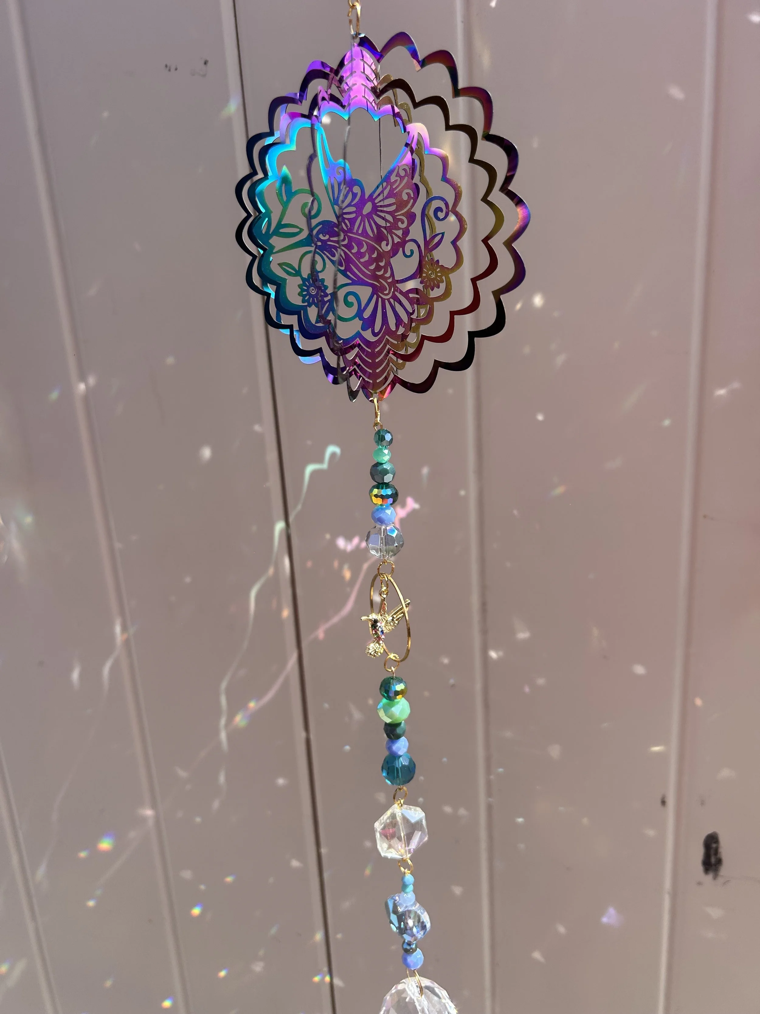 Hanging decorative ornament with colorful beads and a butterfly and fairy design, reflecting light and casting rainbow shadows against a neutral background.
