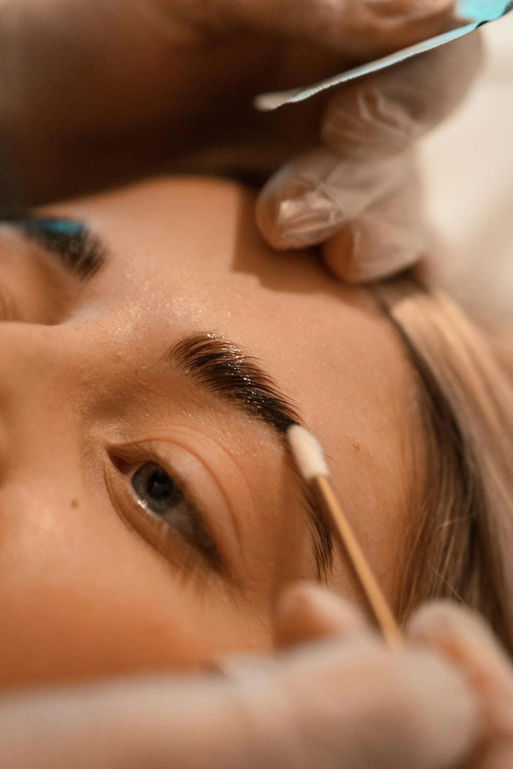 Close-up of a woman with blue eyes getting her eyelashes mascaraed in a beauty salon or makeup area.