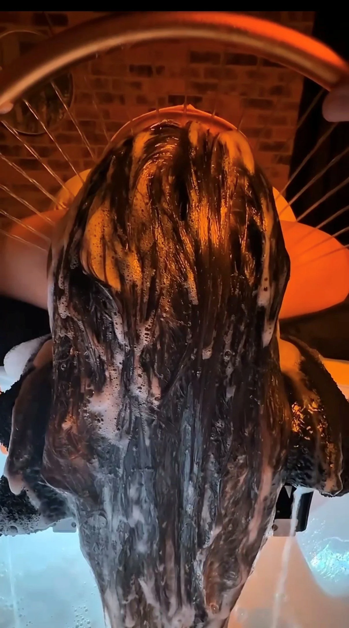Person with long hair covered in black and white soap suds, bathing in a bathtub.