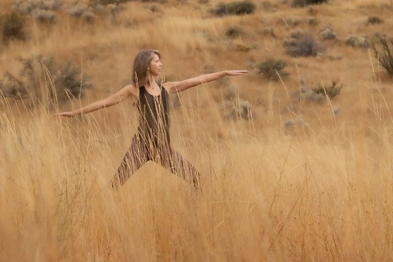 A woman practicing yoga in a field of tall, golden grass with a desert landscape in the background.