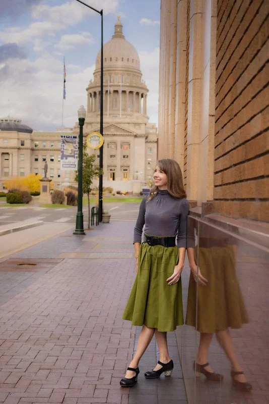 Woman standing on a brick sidewalk with the state capitol dome in the background, leaning against a reflective brown brick wall.