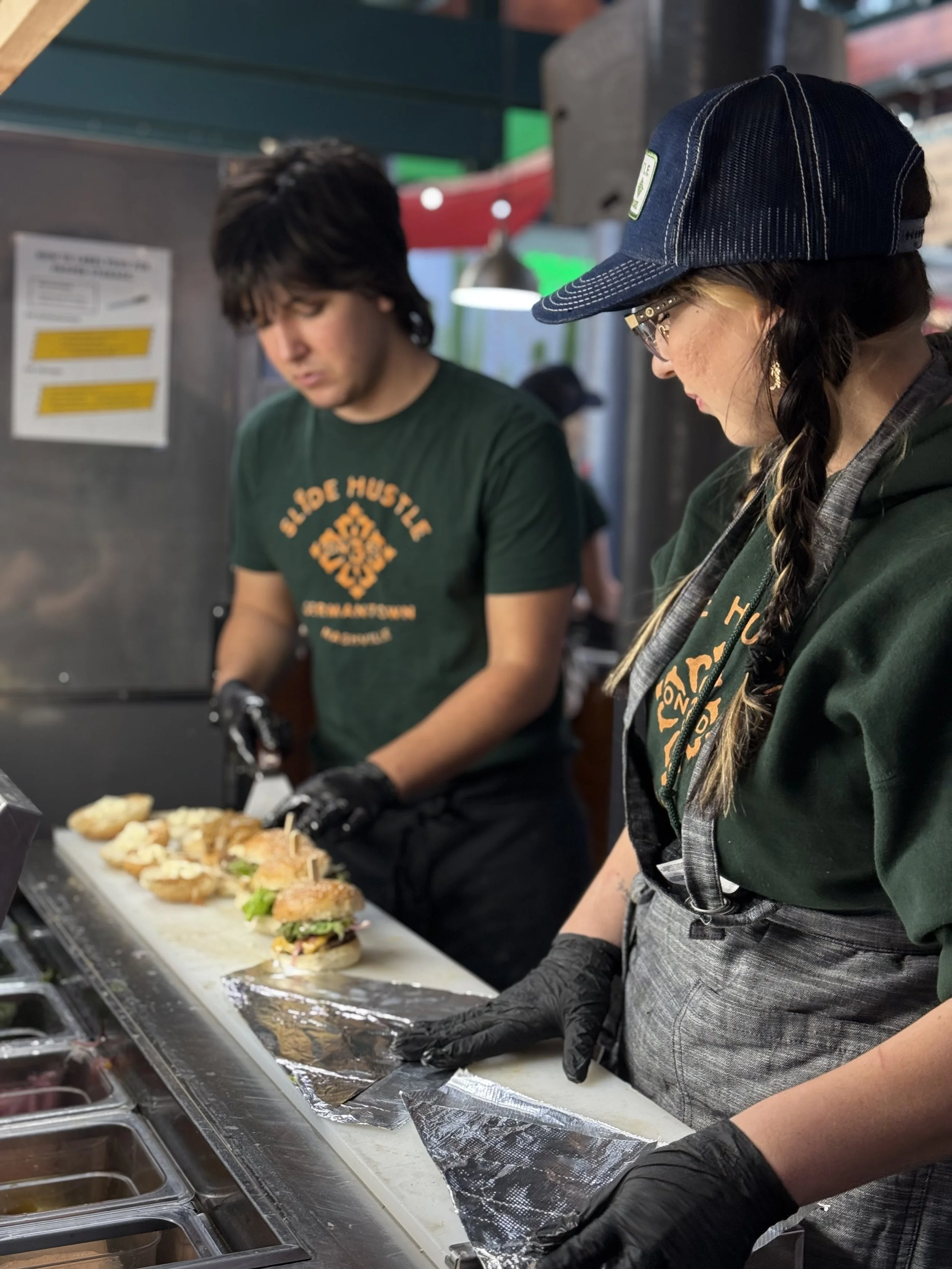 People preparing and serving sandwiches at a food counter in a restaurant or event setting.