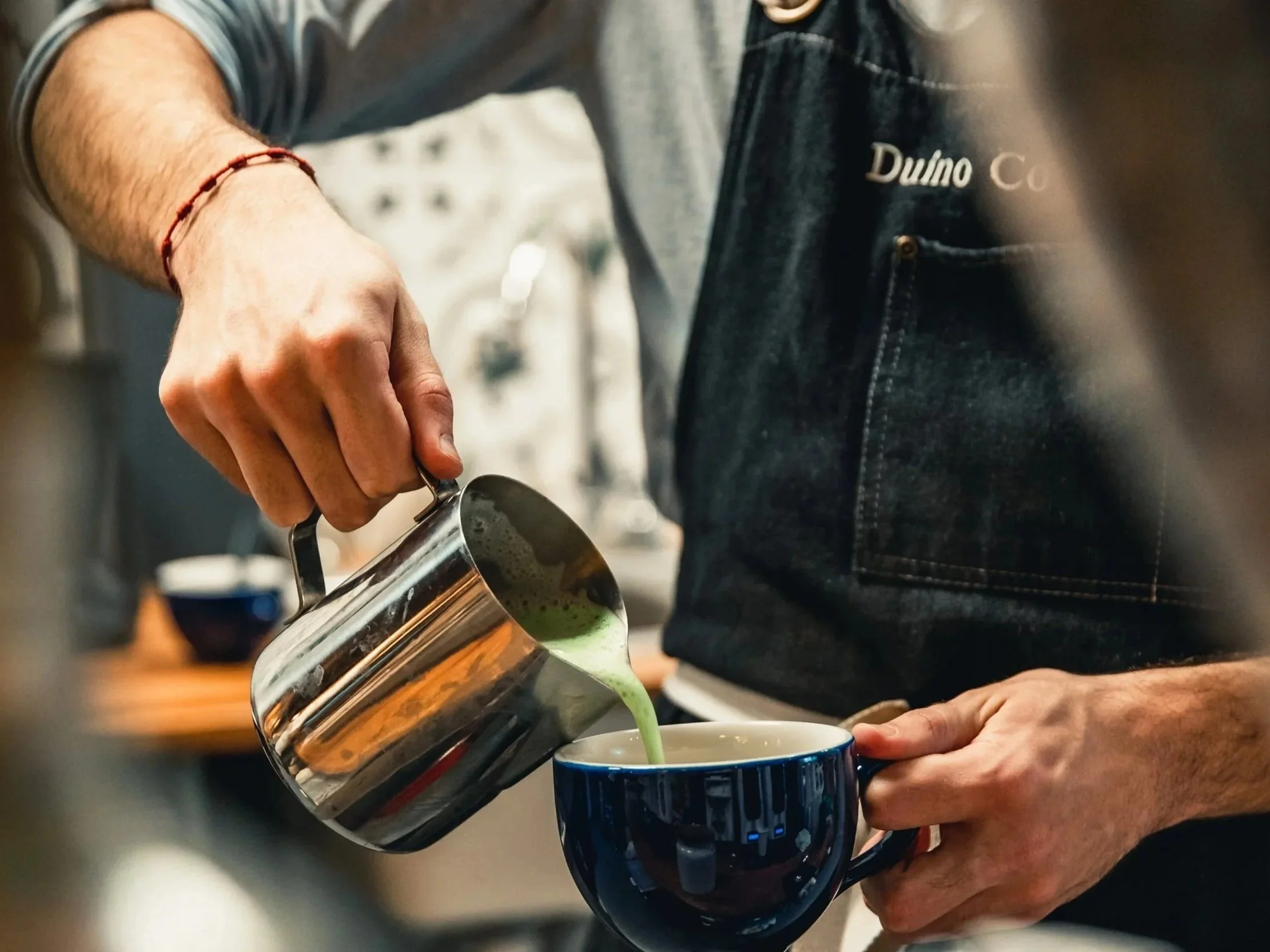 A Duino Barista pouring matcha latte into a cup.