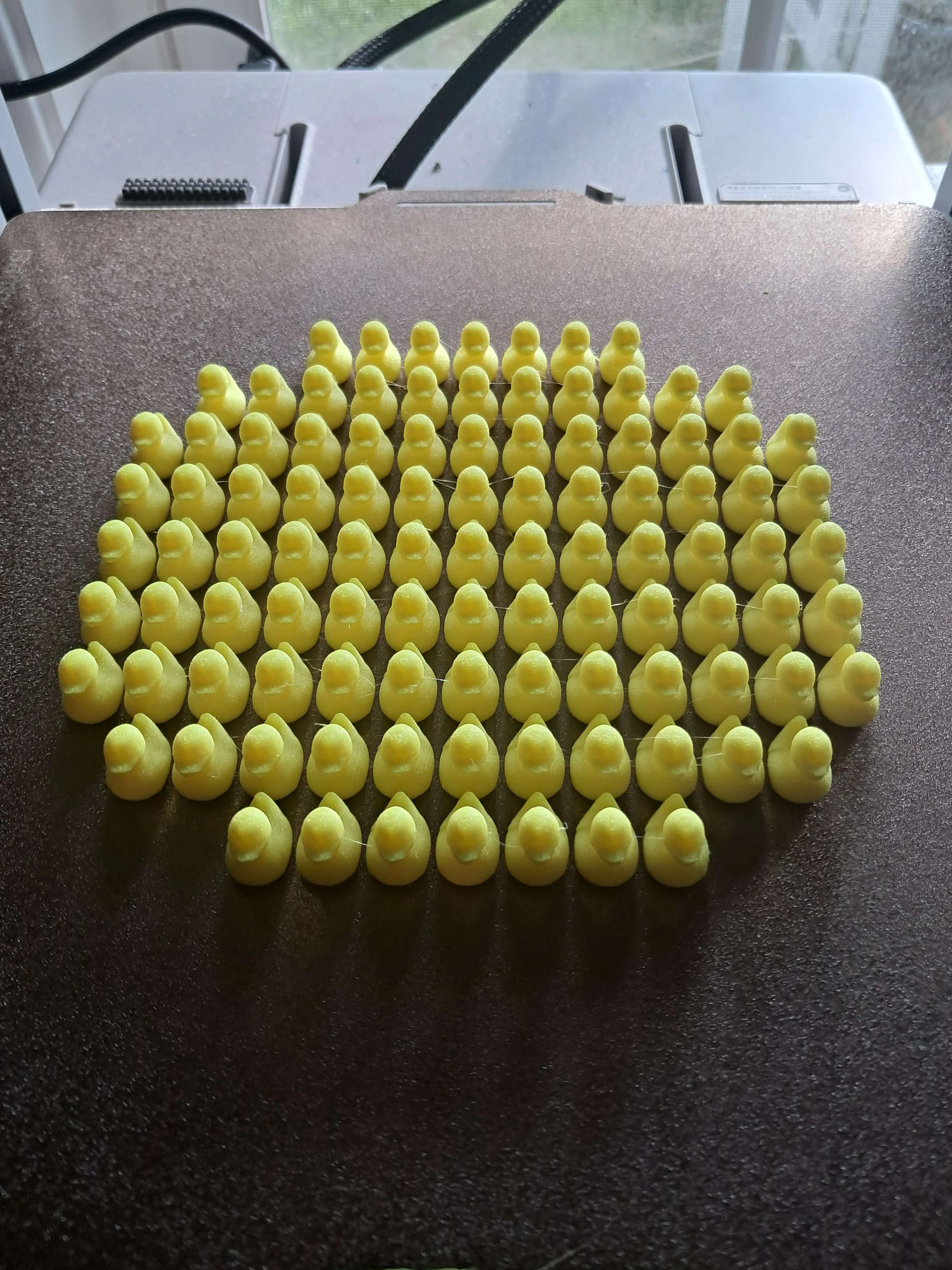 Rows of small yellow rubber ducks on a black surface.