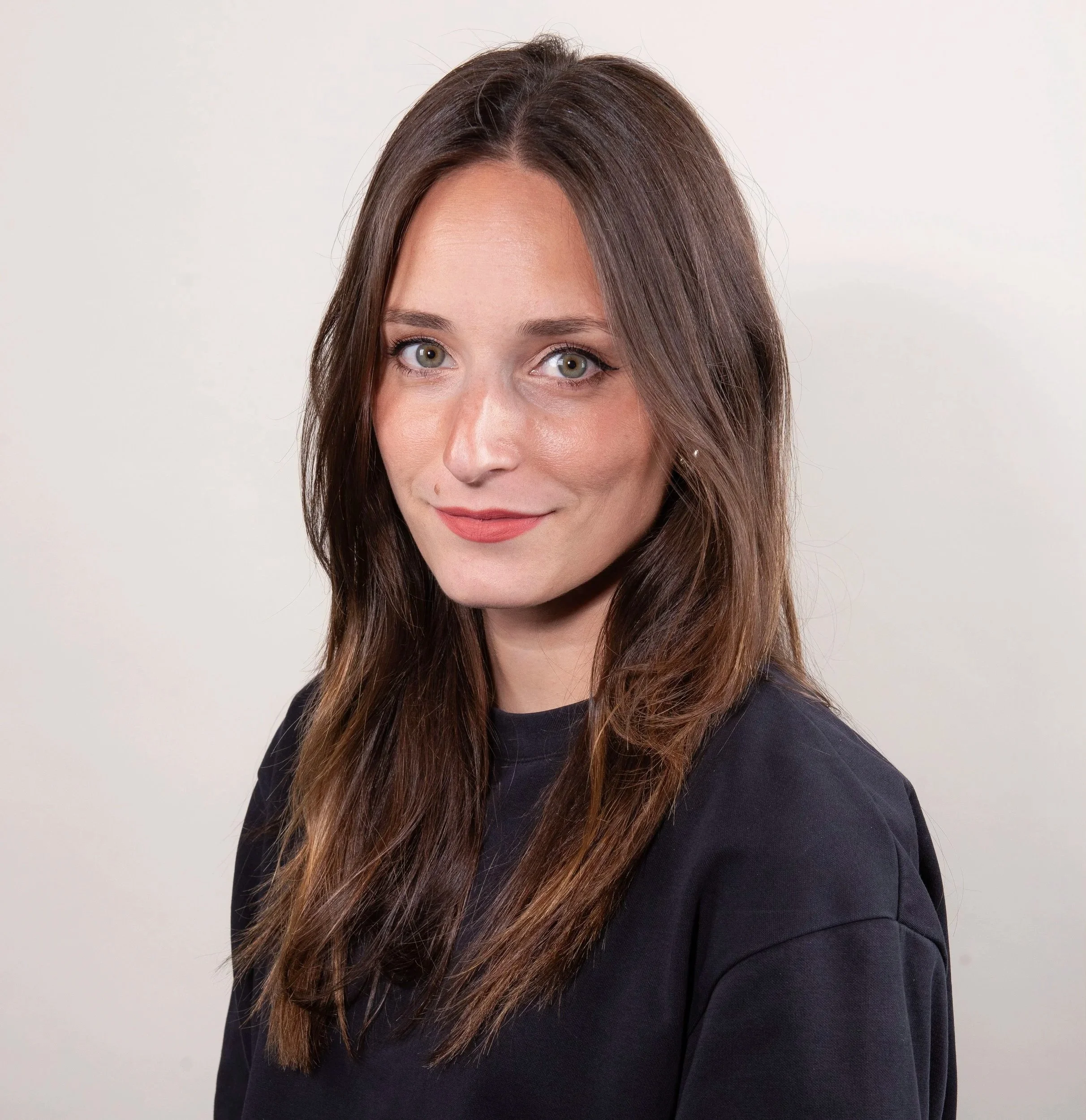 Portrait of a woman with long brown hair, green eyes, sun-kissed skin, wearing a dark top with a white background.