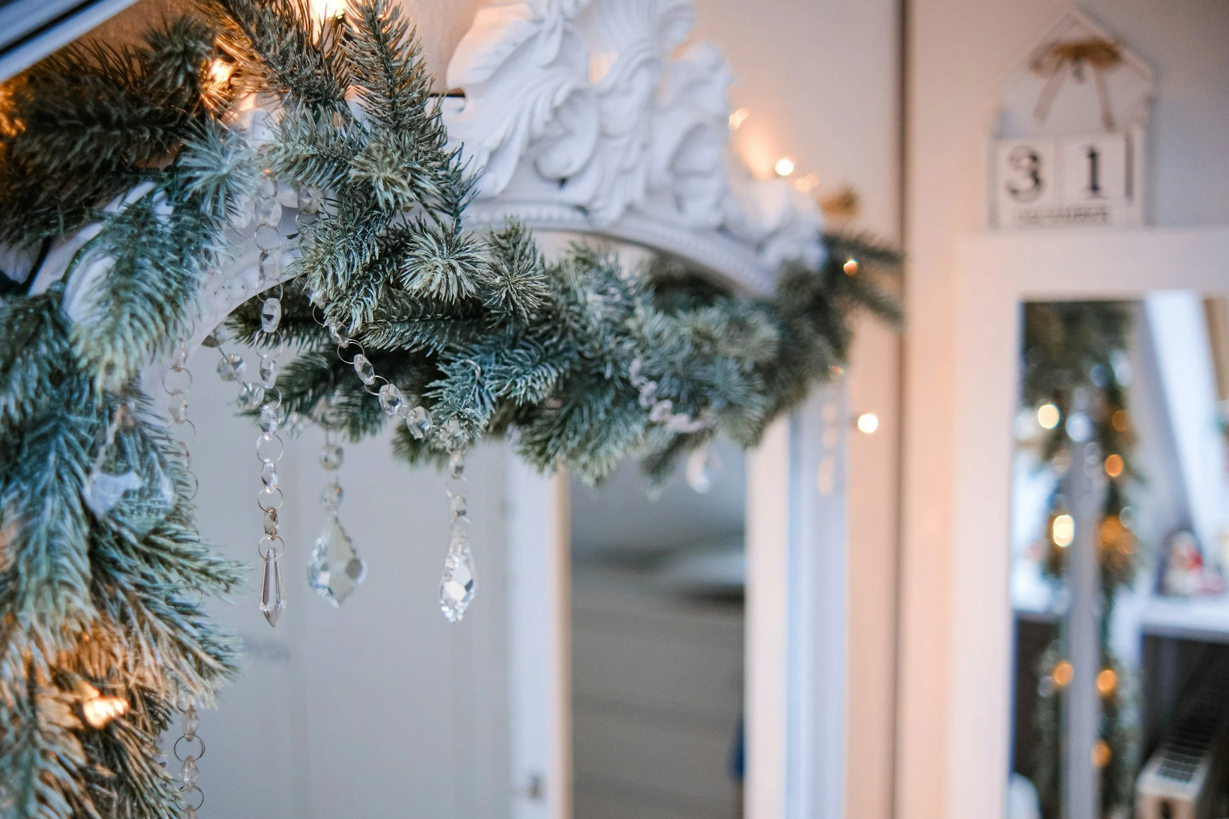 Elegant evergreen Christmas garland with warm lights and ornaments decorating a neutral fireplace mantel