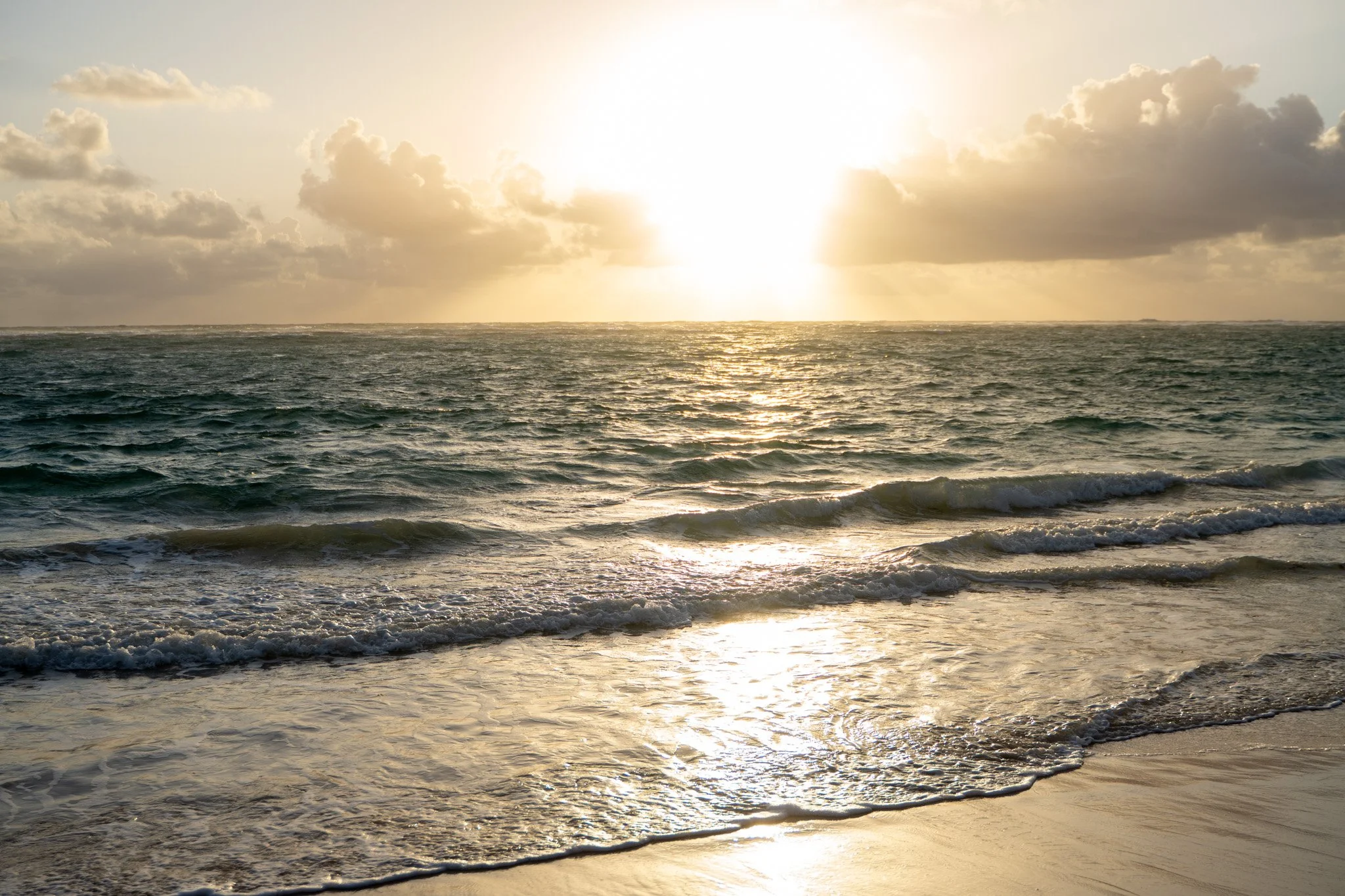 Sunset over the ocean with waves and partly cloudy sky.