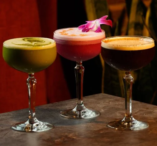 Three handcrafted signature cocktails served in coupe glasses at By The Wayside cocktail bar in East End Houston