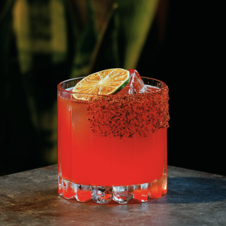 Handcrafted signature red cocktail garnished with dried lime wheel and chili rim at By The Wayside cocktail bar in East End Houston