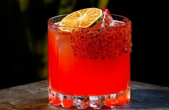 Handcrafted red cocktail with chili rim and lime slice garnish at By The Wayside bar in East End Houston