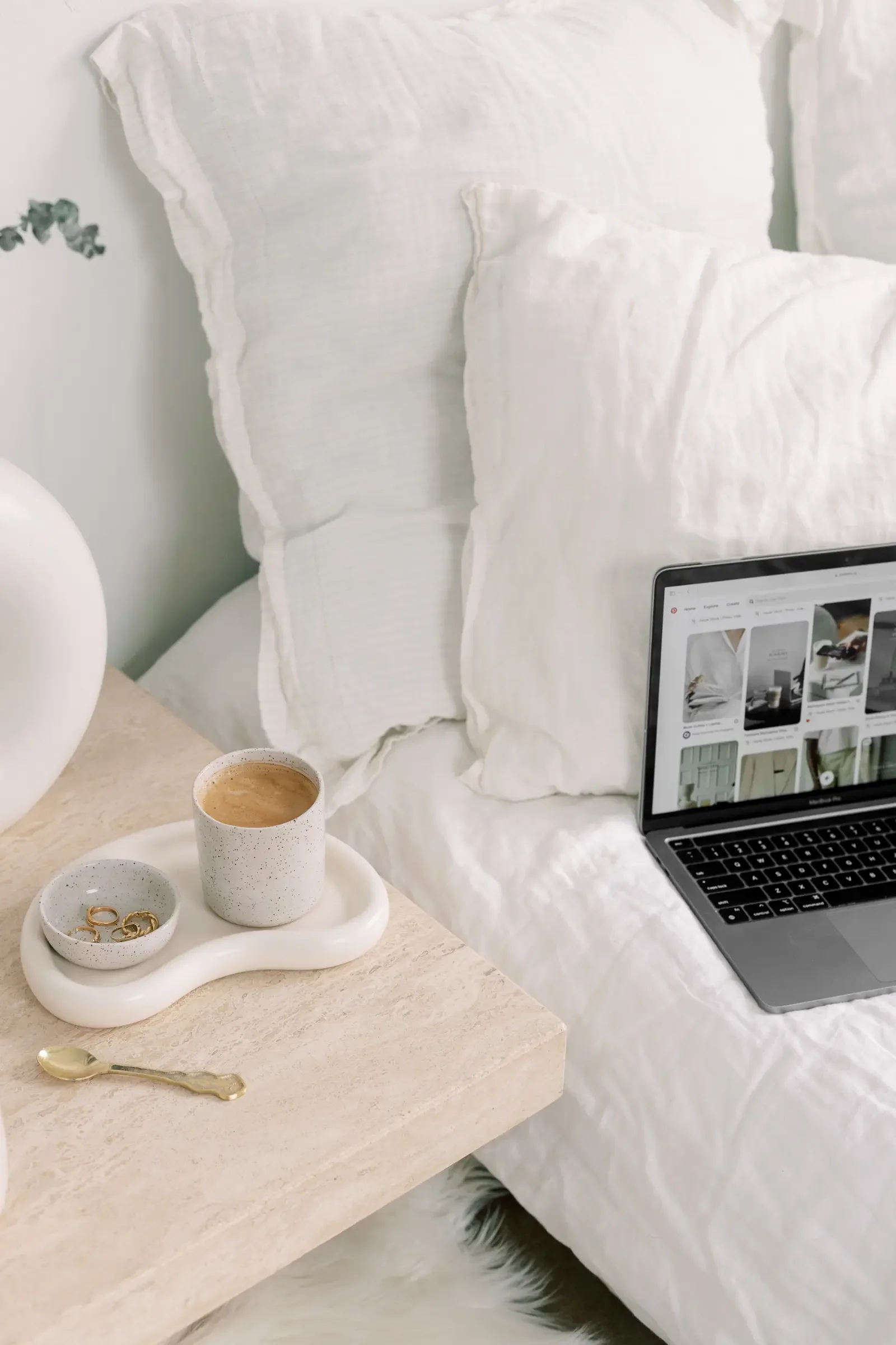 A cozy workspace with laptop placed on a bed and coffee on a bedside table
