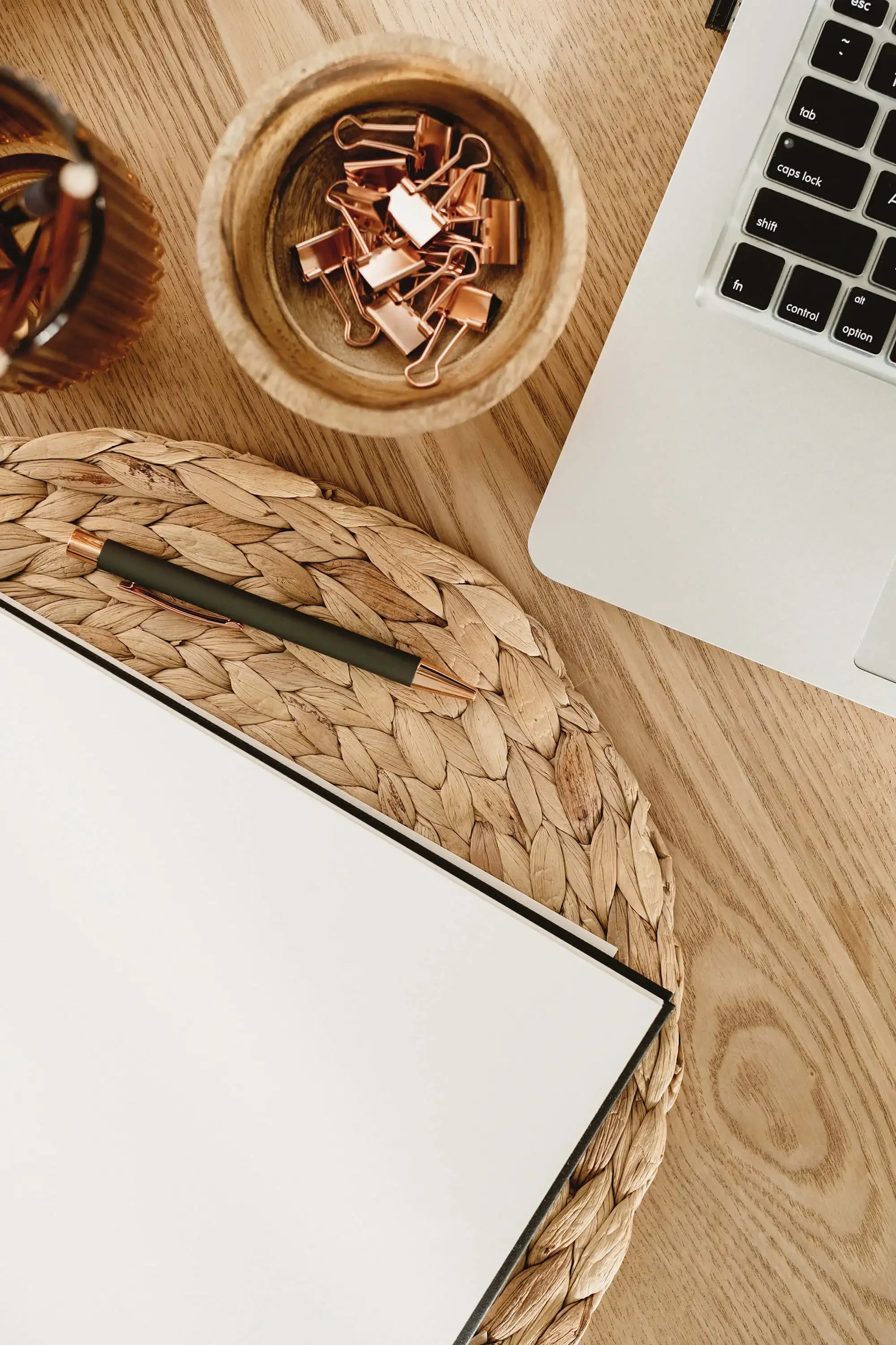 corner of a laptop, a bowl with paperclips and notebook seen from above