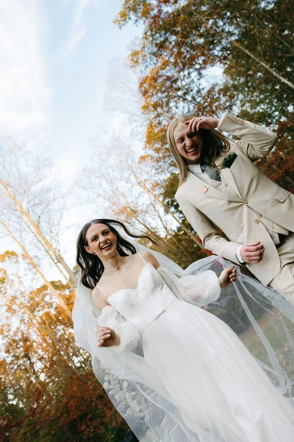 A happy bride and groom celebrating outdoors in an autumn setting with colorful fall trees in the background.