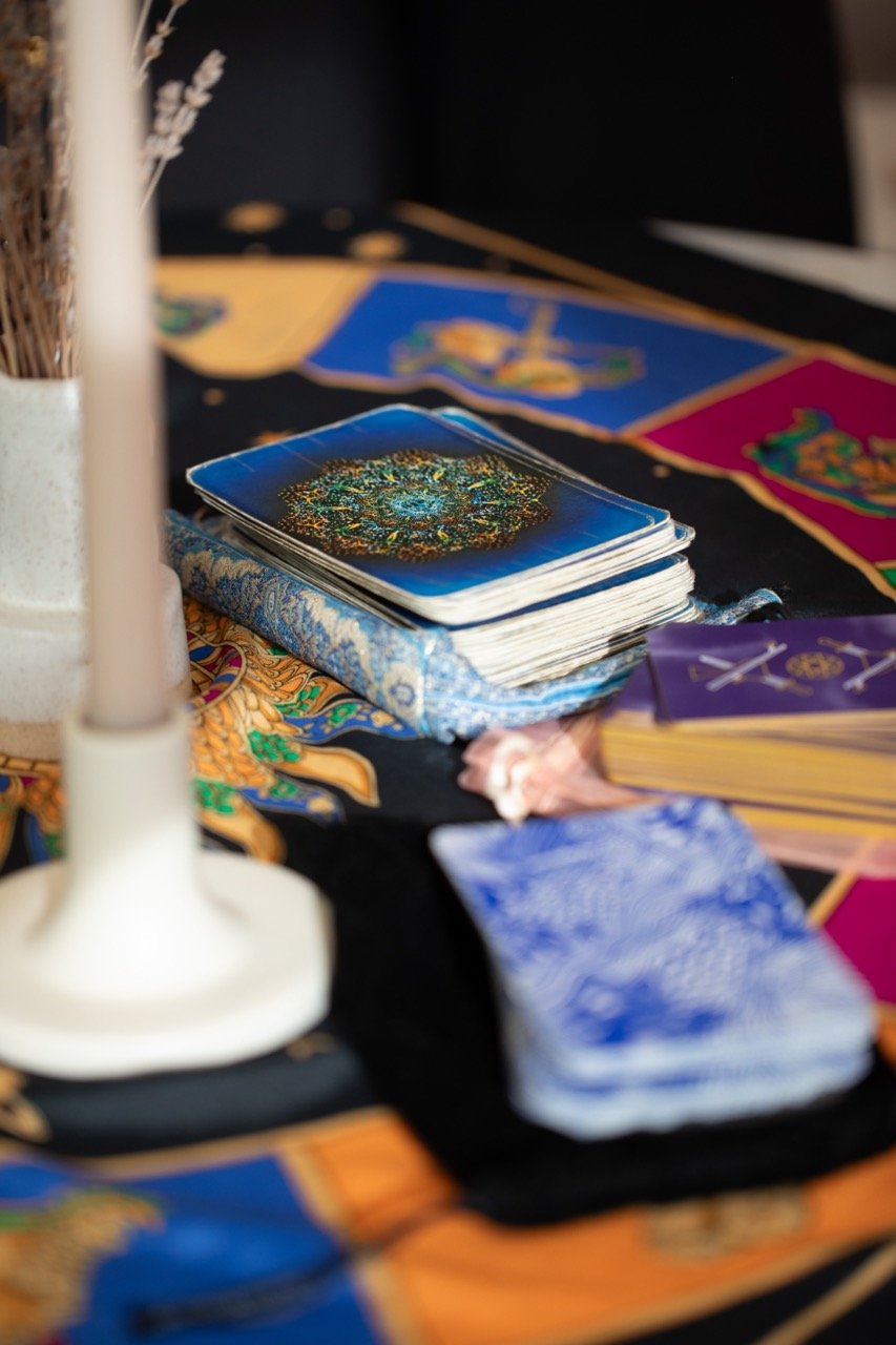 Tarot cards spread out on a decorated cloth with a candle and dried lavender on a table.