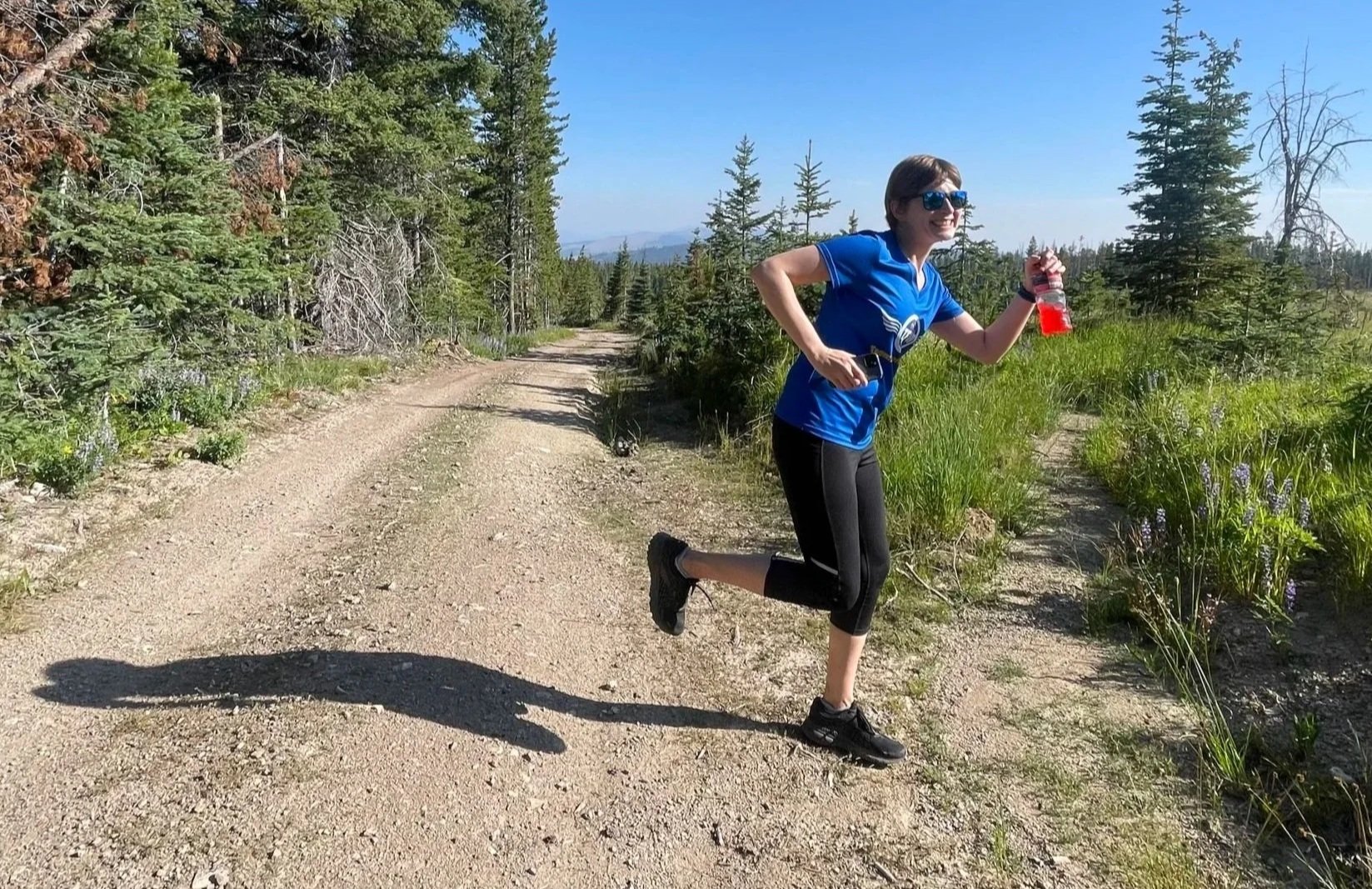 Coach Elena posed mid-stride facing the camera on a trail with a well-defined path and path less traveled