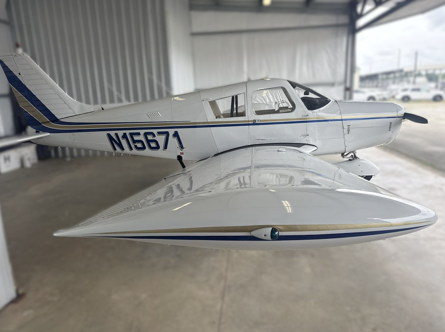 Small white aircraft with blue and gold stripes inside a hangar, with a photo of a missile in the foreground.