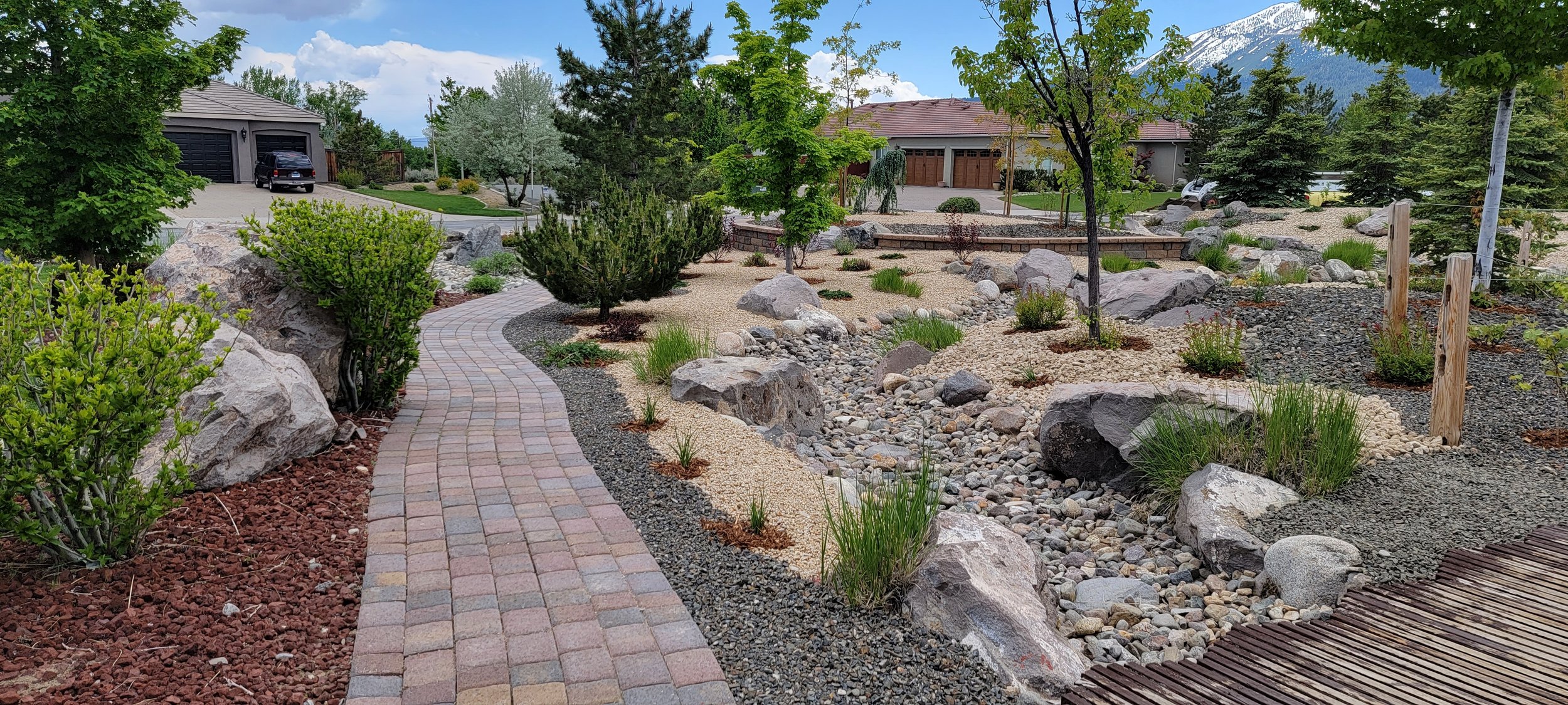 Residential landscape featuring a paver walkway, dry creek bed, decorative boulders, and drought-tolerant planting