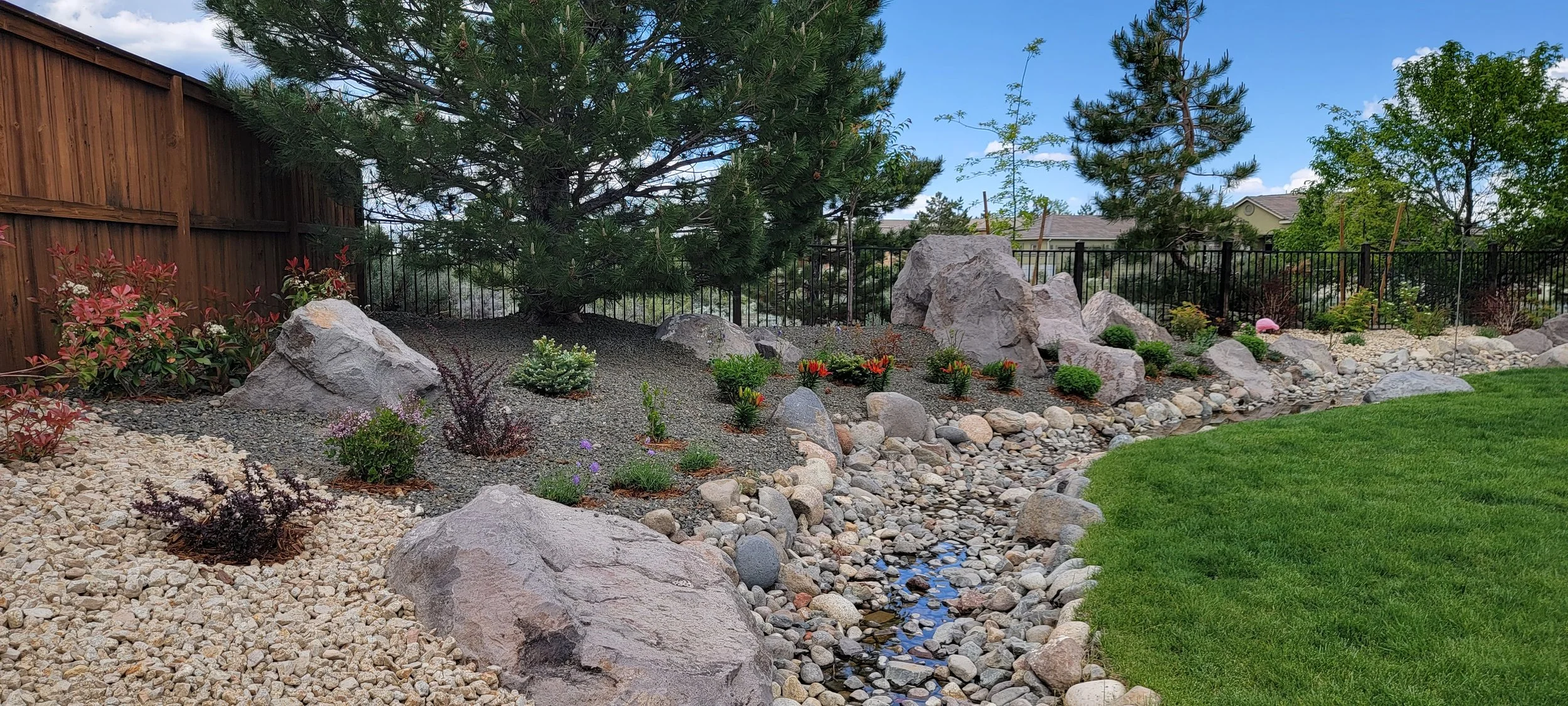 Residential landscape featuring decorative boulders, a dry creek bed, drought-tolerant planting, and a naturalistic garden design