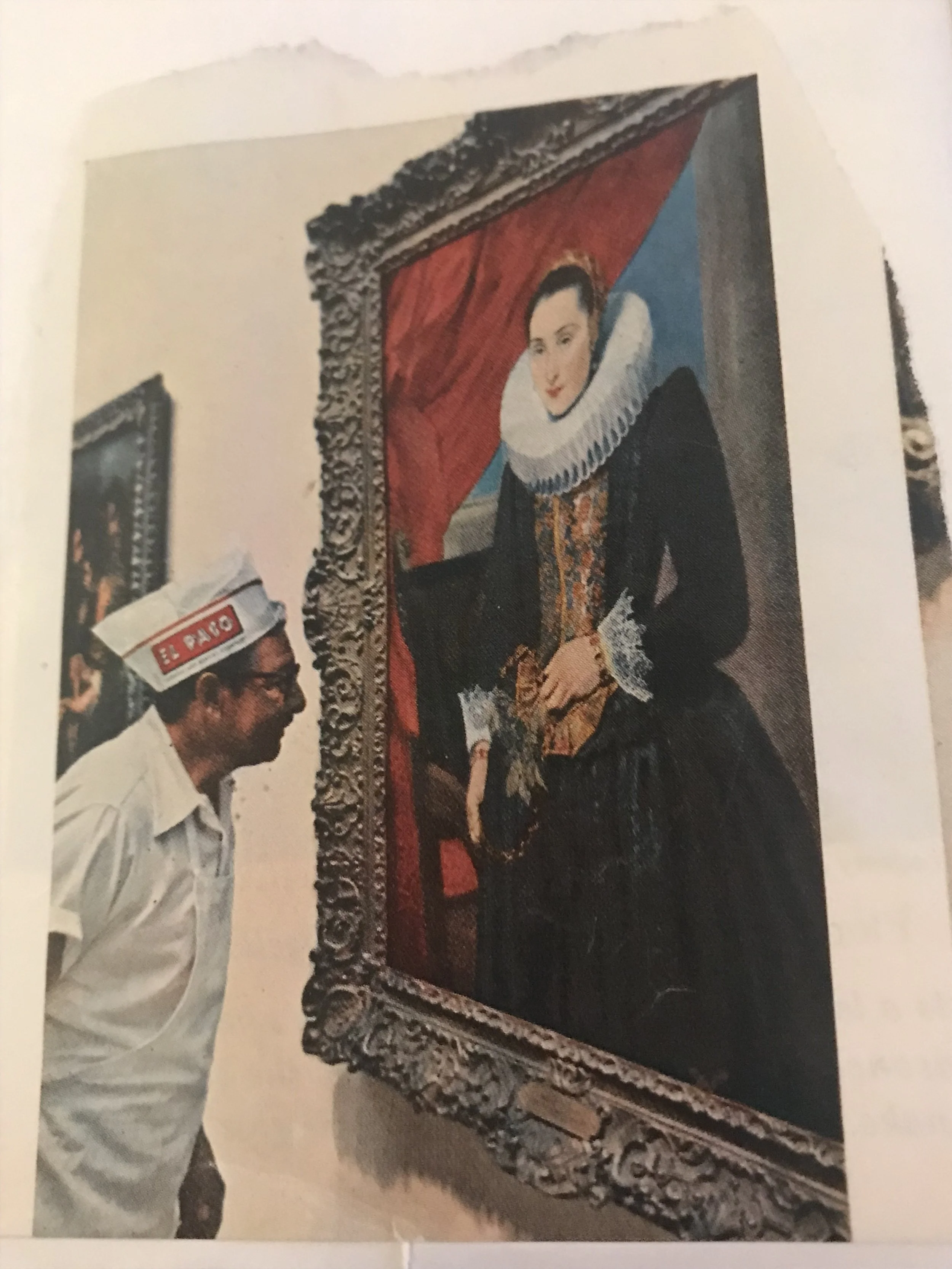 A man wearing glasses and a hat with a red and white logo reading 'El Paso,' standing next to a framed portrait of a woman in historical attire, with elaborate jewelry and clothing, displayed on the wall.