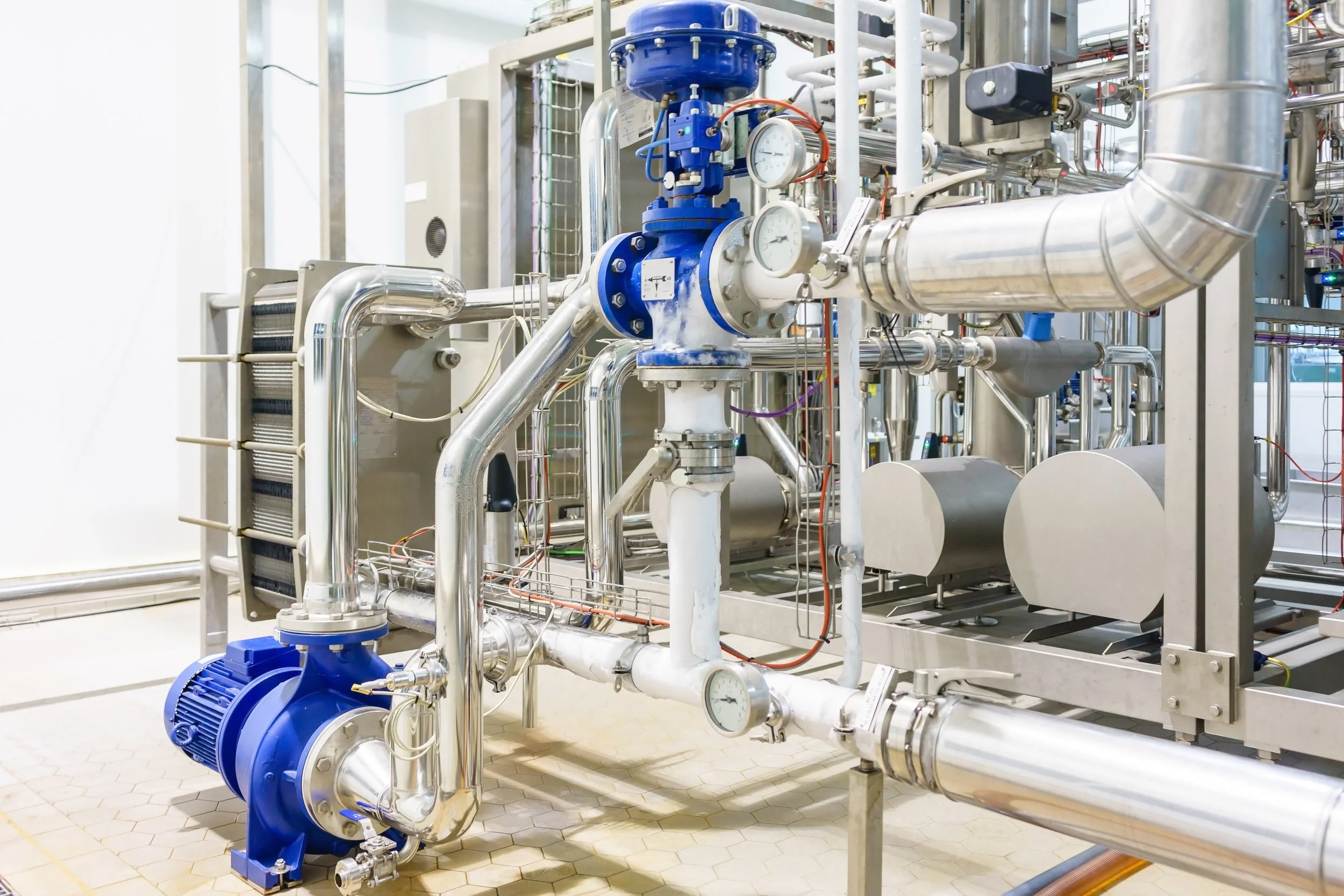 Industrial machinery with pipes, gauges, and a blue motor in a clean industrial setting.