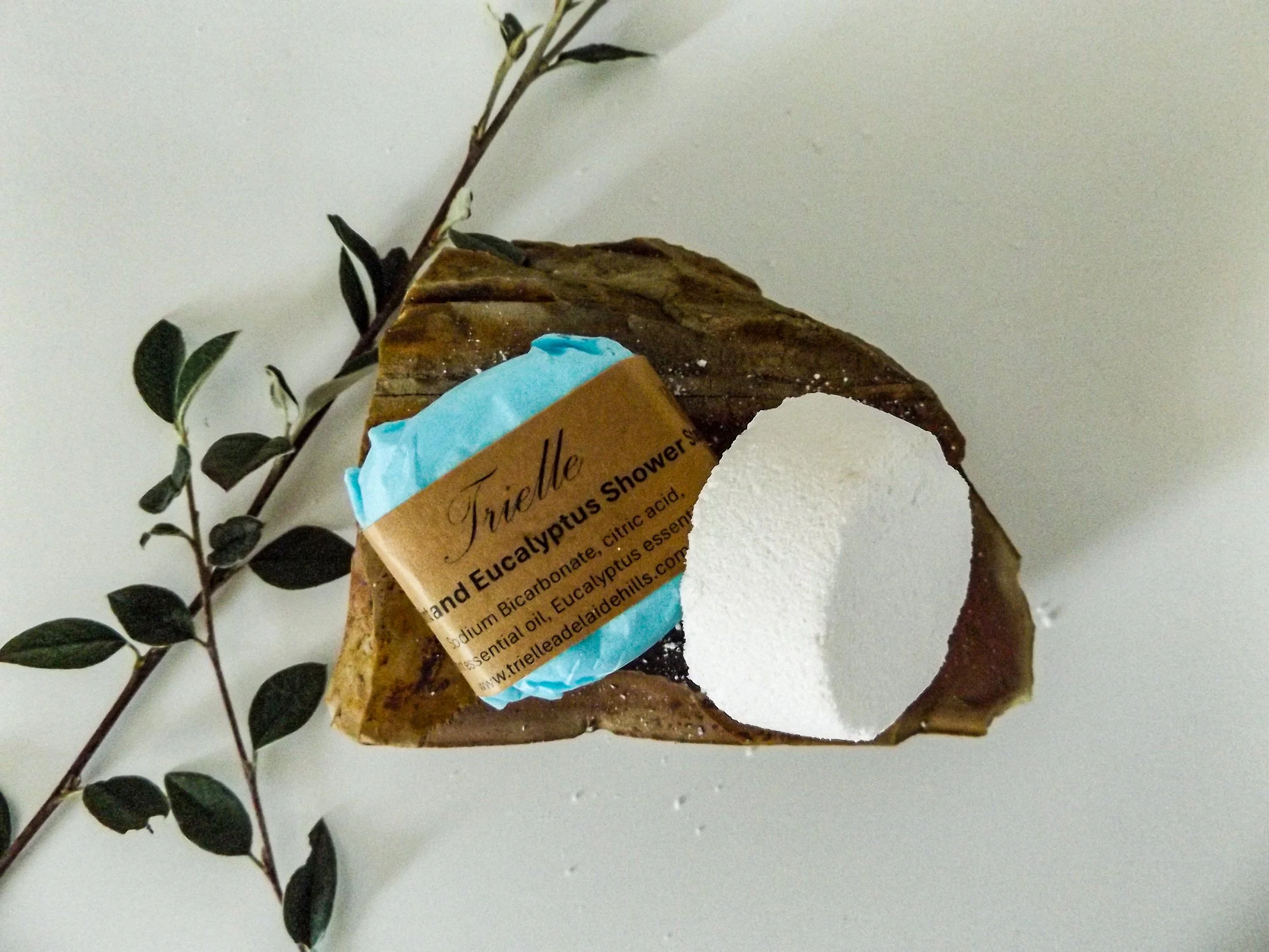 A soap with a label that reads 'Trielle' and contains eucalyptus essential oil, placed on a white surface with a small green leafy branch next to it.
