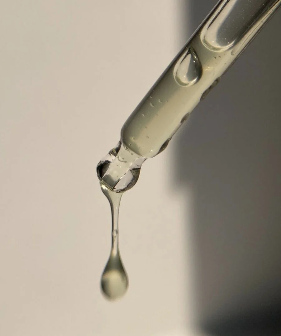 Close-up of a glass pipette with a droplet of clear liquid hanging from its tip.