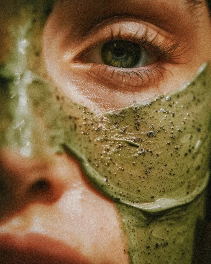 Close-up of a woman with green eyes wearing a green facial mask with small black specks.
