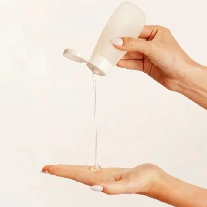 Person holding a bottle of liquid soap or lotion above a palm with some of the liquid pouring onto it.