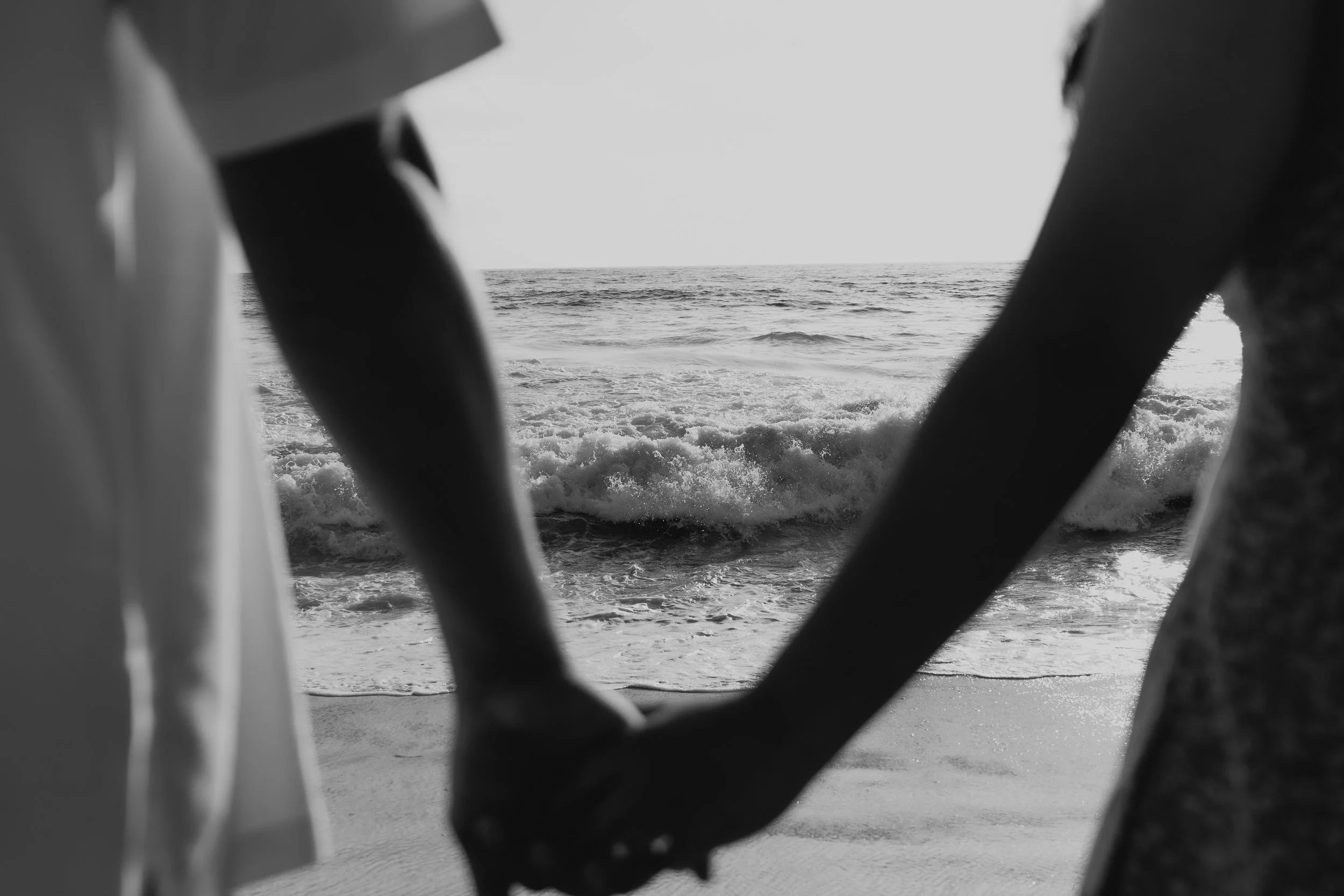 Black and white photo taken from behind a boat's railing, showing the ocean with small waves and a cloudy sky in the background.