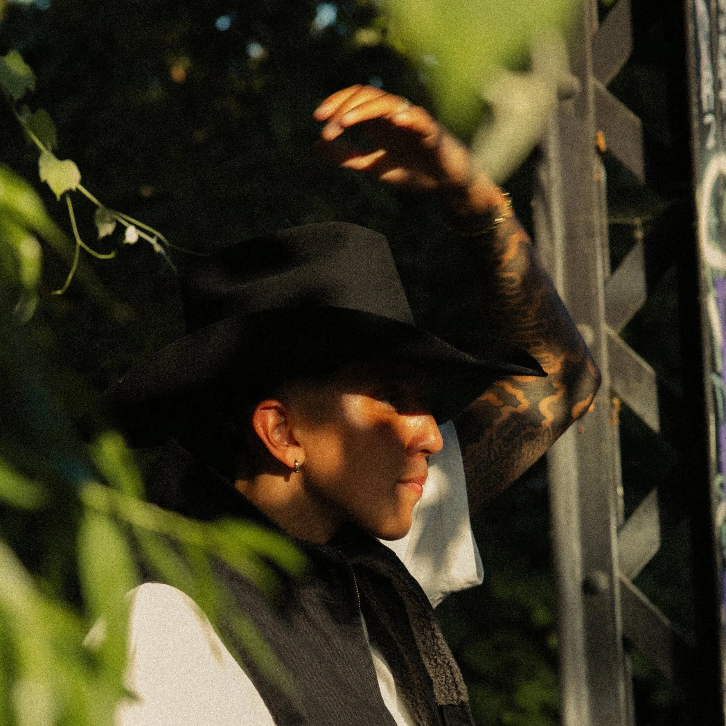 Close-up of a person with earrings and a ring, holding a mobile phone, sitting in a green outdoor area with blurred greenery in the background.