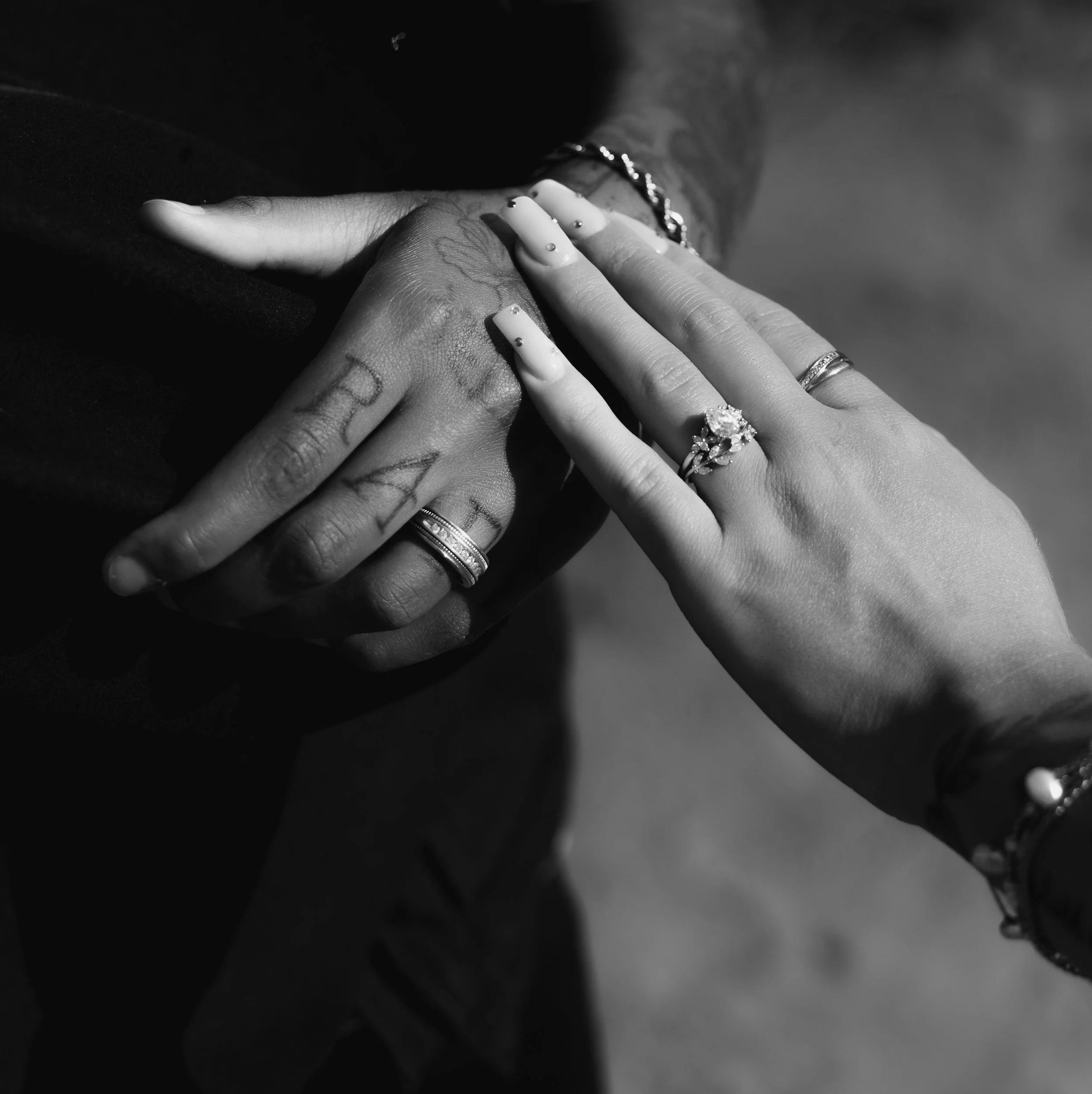 Black and white close-up photograph of multiple hands stacked, with various rings and a bracelet, suggesting a moment of unity or celebration.