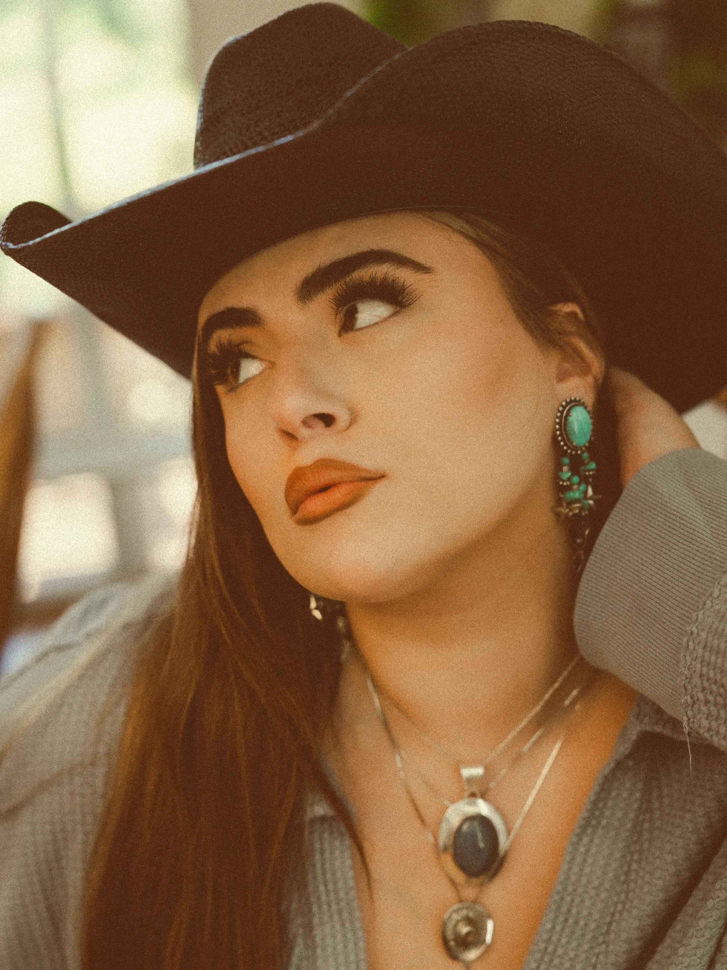 Close-up of a woman wearing a brown cowboy hat, turquoise earrings, and layered necklaces.
