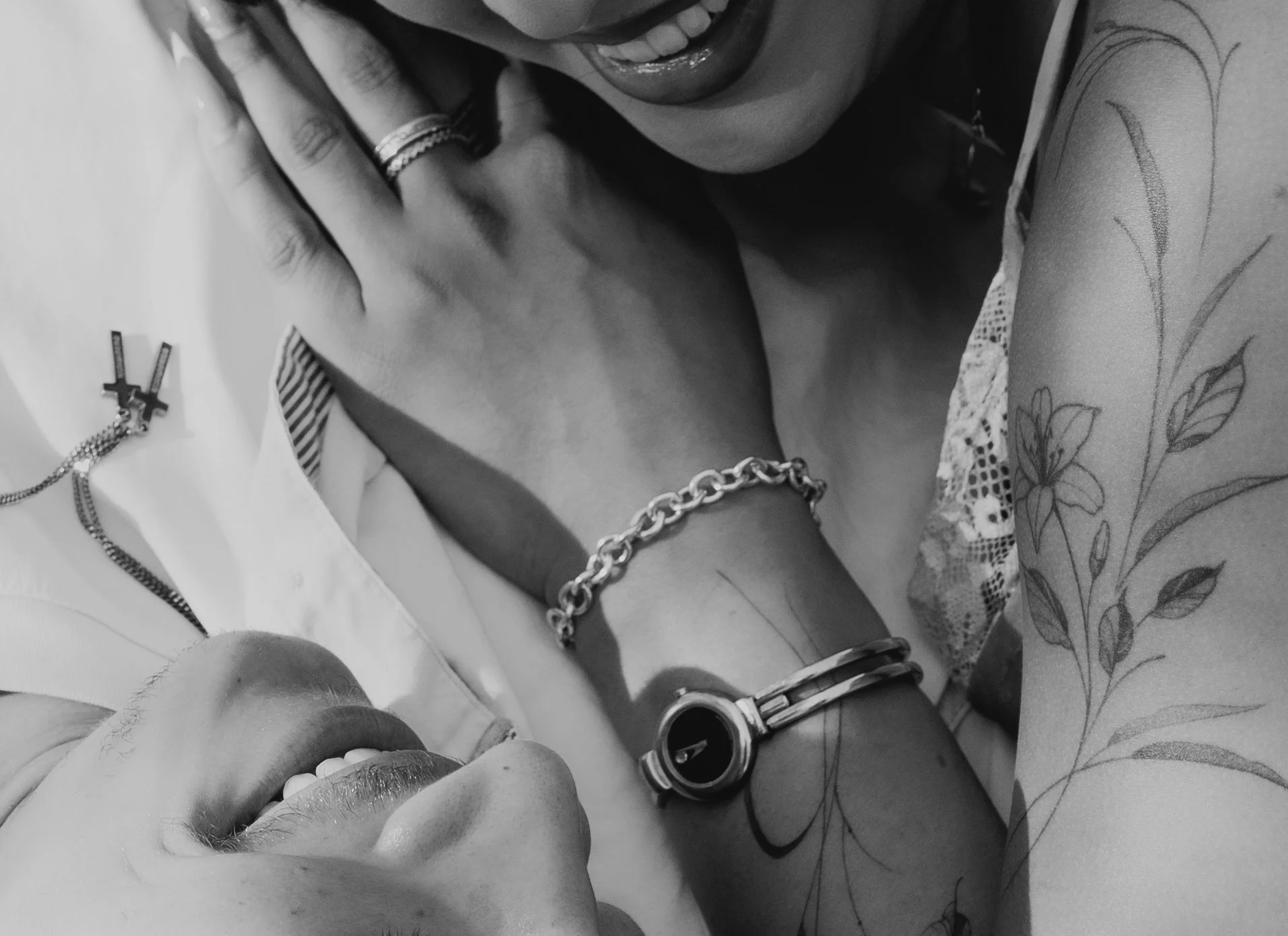 Close-up of people wearing jewelry, including rings, bracelets, a watch, and a necklace, with floral tattoo on arm, all in black and white.